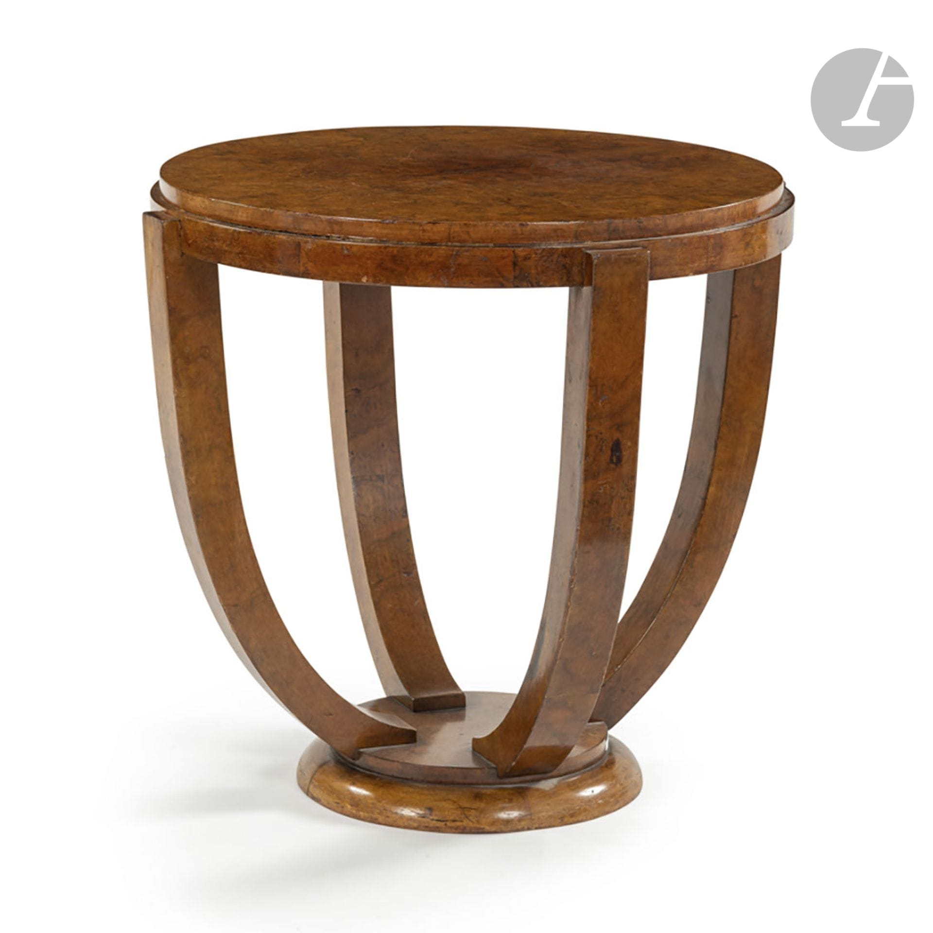 TRAVAIL DES ANNÉES 1930
Guéridon en placage de loupe. La base à un gradin reçoit les quatre jambages curvilignes soutenant le plateau circulaire. État d’usage. H. 65 cm – D. 69 cm