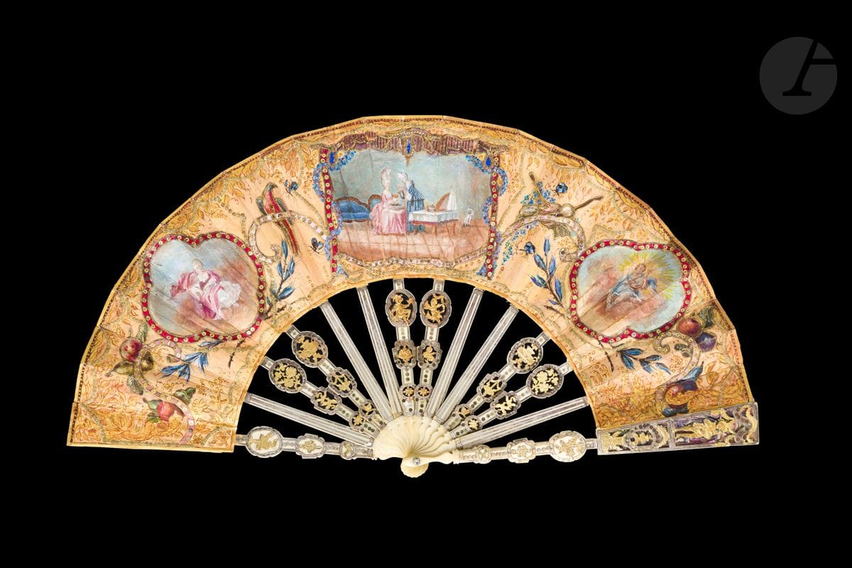 L’heure de la toilette, Europe, vers 1760-1770
Éventail plié, la feuille en soie, doublée de papier, et peinte de trois cartels parmi des fruits, des oiseaux exotiques, des instruments de musique. Les papillons sont rehaussés en plumes naturelles. À gauche, Vénus sur une nuée, Apollon et sa lyre à droite. Au centre, une femme de chambre et une dame de qualité à la toilette. 
Paysage esquissé au revers.
Monture en ivoire* découpé, gravé et doré à décor de fleurs, vases et personnages. Les panaches rehaussés de nacre haliotide. 
H.t. 26,8 cm-H.f. 12 cm (usures, importantes restaurations). 
Poids brut : 110 g