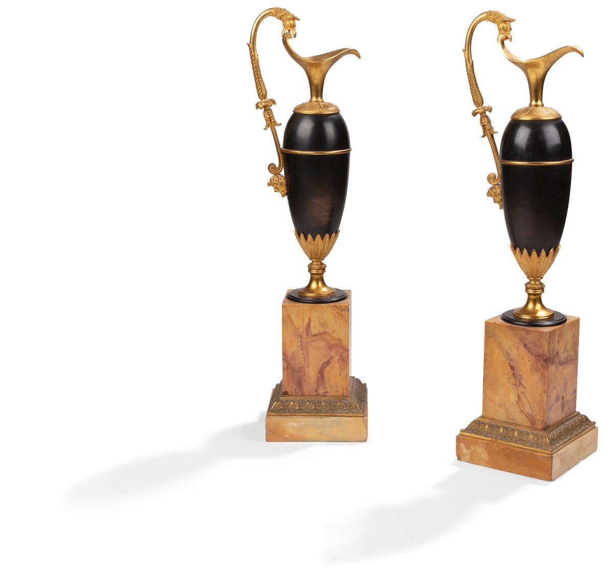 *Paire d’aiguières en bronze patiné et bronze doré, les anses à tête de griffon, reposant sur une base en marbre jaune de Sienne et un contre-socle en bronze doré à décor de frise feuillagée ; (restaurations).
Première moitié du XIXe siècle.
H : 51 cm