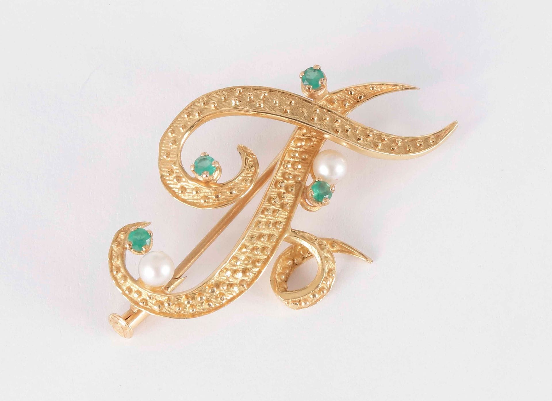 Broche en or 18K (750) formant la lettre F, ornée de pâtes de verre vertes et de perles de culture. 

Poids brut : 6,2 g