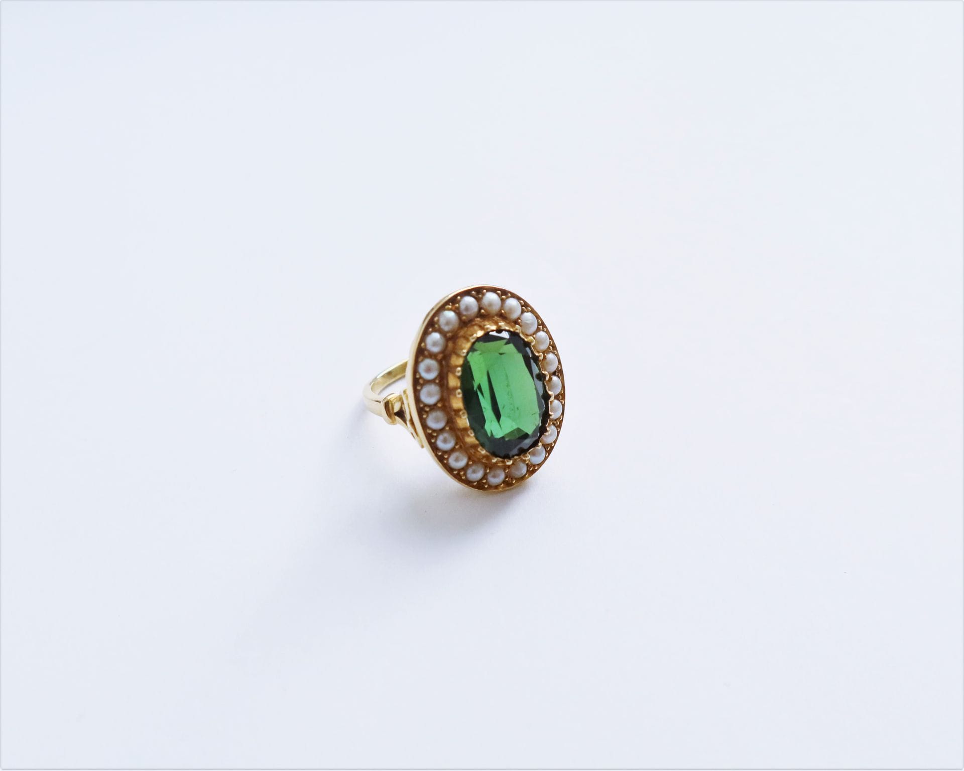 Bague en or 18K (750), sertie d'une tourmaline verte de forme ovale entourée de demi-perles. Travail de la fin du XIXe siècle. tour de doigt : 52. Poids brut : 11,3 g (égrisures)