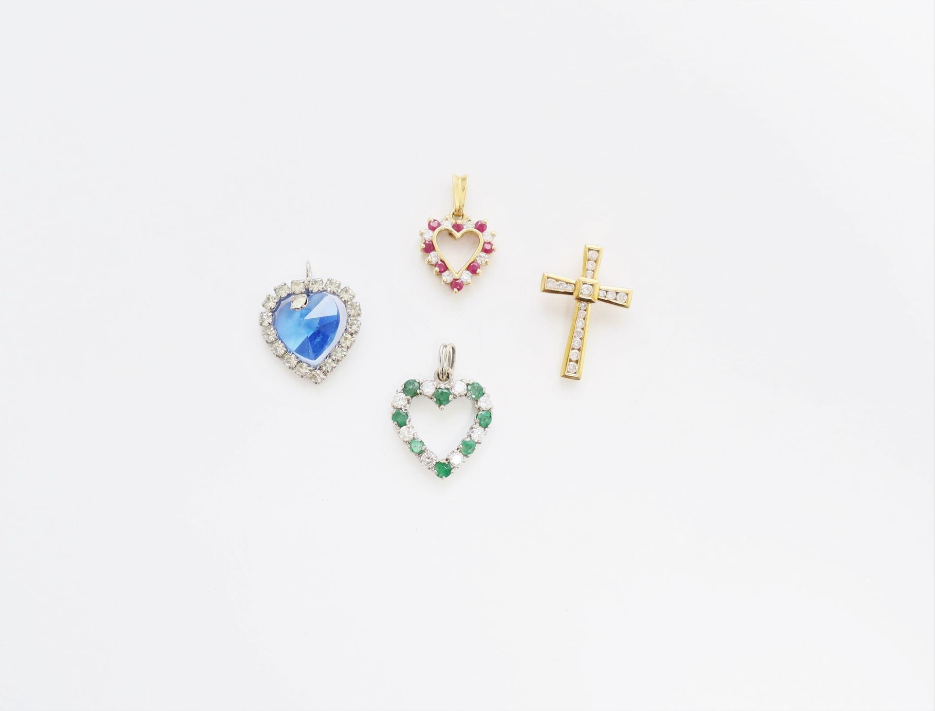 Lot de 3 pendentifs en or 18K (750): l'un en forme de croix sertie de diamants, les deux autres cordiformes sertis de diamants et d'émeraudes ou de pierres blanches et rubis. Poids brut : 5,2 g (on joint un pendentif cordiforme fantaisie)