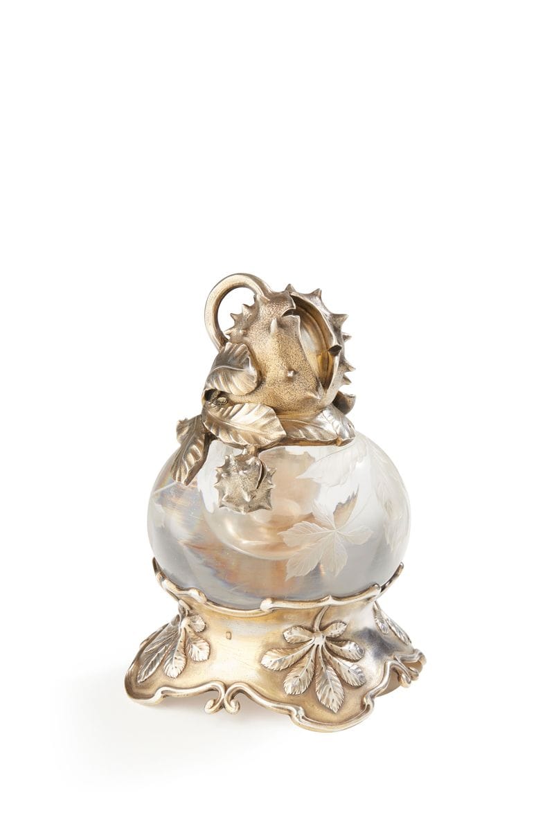 FRANCE ART NOUVEAU
Encrier en cristal taillé et sa monture en vermeil de forme circulaire. Le piédouche polylobé est ciselé de feuilles de marronnier, le corps gravé de bogues, le couvercle ouvrant à charnière figure une grosse bogue à peine ouverte sur sa terrasse de feuilles et une plus petite sortant des feuilles.
Poinçon minerve
Orfèvre : M un marteau à rétreindre et deux étoiles au dessus
Poids brut : 1492,6 g - hauteur : 15 cm