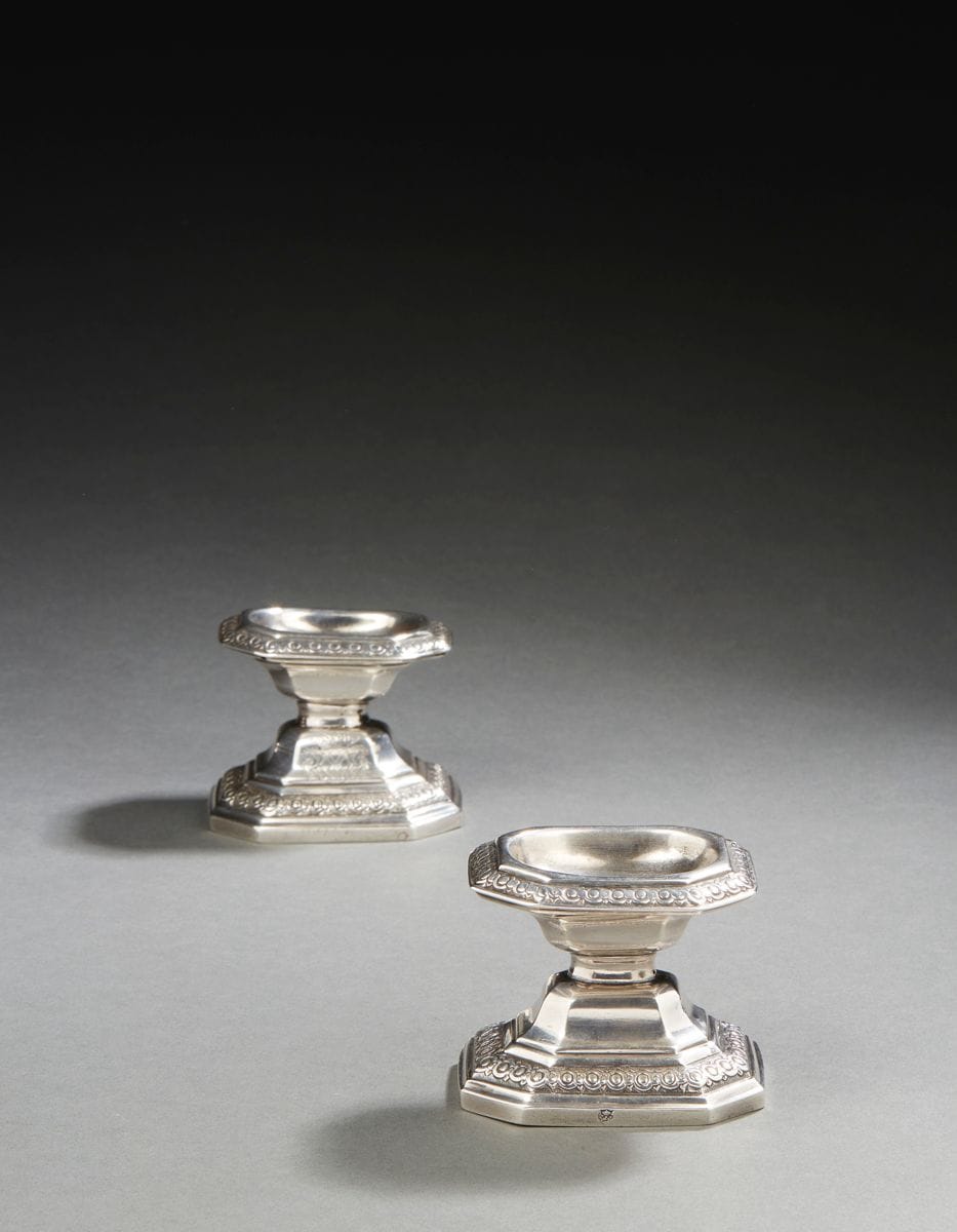 RENNES 1725 - 1726
Paire de salières en argent. Rare modèle français rappelant celui des salières de Liège dites «diabolo». Elles reposent sur une base hexagonale à pans coupés en rappel sur la bordure supérieure, repoussée d’oves et d’entrelacs sur un fond amati. La partie inférieure sur les doucines est gravée des armoiries de jeune fille de René-Caroline-Victoire de Froulay (1714 - 1803), mariée en 1737 au marquis de Créquy (1686 - 1741). Elle tint salon à Paris durant tout le XVIIIe siècle.
Maître orfèvre : Jacques-Eloy PIGEON, reçu en 1725
Poinçons : poinçonnée deux fois du maître orfèvre dans le fond et la base, décharge entre 1722 et 1726.
État : deux petits trous aux deux angles supérieurs d’une salière
Poids : 219 g - hauteur : 6,5 cm - longueur : 8 cm - largeur : 6,5 cm