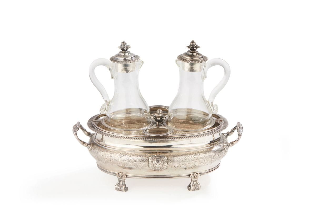 TOULON 1737
Huilier-vinaigrier en argent, complet de sa grille et se ses bouchons (carafes en verre postérieures). De forme bassin, reposant sur quatre pieds à enroulements fleuronnés, le corps est gravé ciselé sur un fond amati de rinceaux et fleurons encadrant des oiseaux tournés vers la gauche. Deux médaillons rapportés de part et d’autre, l’un est dégravé d’armoiries, le second figure un mascaron de face. La bordure est moulurée de godrons en rappel sur les bouchons terminés par des graines en panache. Deux anses latérales rapportées en argent fondu forment de doubles accolades.
Maître orfèvre : Nicolas II BOULLET, reçu en 1717
Poids : 823,1 g - longueur : 25,5 cm - largeur : 14,4 cm
État : anciennes restaurations à la grille

Provenance : 
A figuré à l’Exposition de Marseille en 2005 - 2006, au musée Grobet-Labadié : « L’orfèvrerie civile en Provence au XVIIIe siècle » sous le numéro 169 - décrit et reproduit page 254 du catalogue.