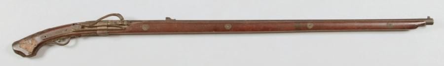 Fusil à mèche japonais dit Teppo. Canon à pans. chien, platine et garnitures en laiton (manques). Crosse en bois incrusté de plaques en laiton découpé. M.E. (Oxydation). XIXe siècle.
