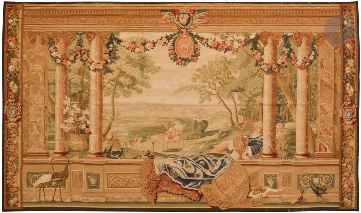 Tapisserie dans le style du XVIIIe siècle d’après un carton des Gobelins de la série des châteaux, et de la série des mois, à décor d’une chasse royale entourée au premier plan d’une balustrade, surmontée de trois colonnes. Un château est très légèrement visible au fond de la composition (Fontainebleau ?) et dans le haut, le signe du cancer est surmonté des armes royales. 
XXe siècle
185 x 319 cm
Couleurs oxydées, bon état