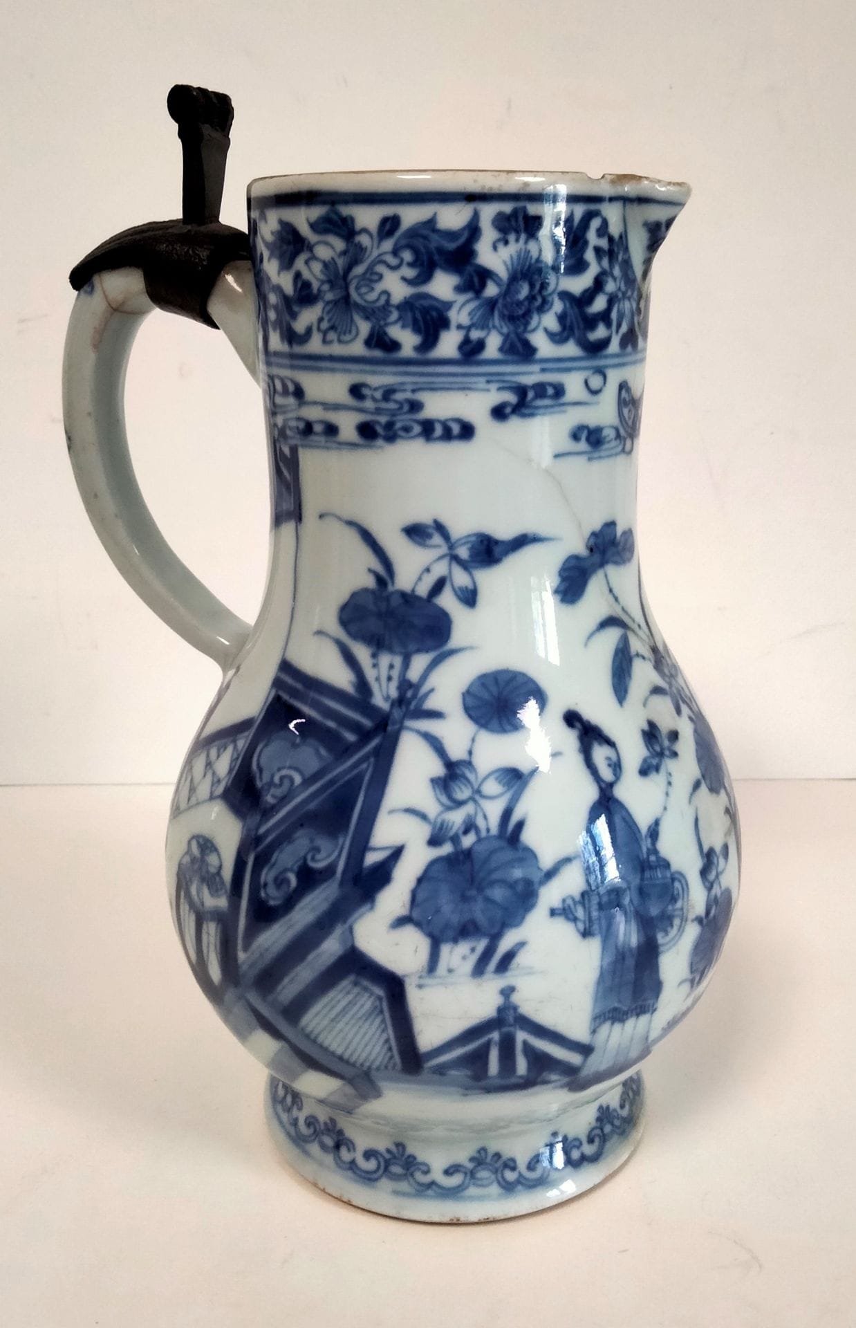 Verseuse en porcelaine bleu blanc, Chine, époque Kangxi (1662 - 1722)
A panse basse à décor de jeunes femmes tenant une branche fleurie dans un intérieur et dans un jardin. Une frise de rinceaux feuillagés et fleuris surmonte les scènes. 
Hauteur : 21 cm
Égrenures, fêlures, restauration à l'anse, éclats, manque le couvercle.