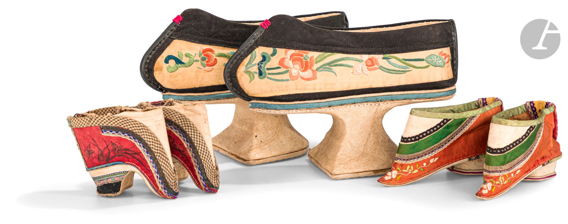 Trois paires de chaussures de femmes, Chine, XIXe - XXe siècle
- Petite paire de chaussures pour pieds bandés en soie polychrome rouge à motif floral et ornée de divers galons gris à motifs de croisillon, bleu, vert et jaune. Longueur : 7,4 cm
- Paire de chaussures pour pieds bandés en soie polychrome brodée de rinceaux fleuris sur un fond orange et décorée de divers galons vert, noir ou violet. Longueur : 12,3 cm
- Paire de chaussures mandchoue qixie de type mati dixie - 馬蹄底鞋 (forme dite de sabot de cheval) en soie noir et beige brodée de feuilles, boutons et fleurs de lotus polychrome. Le talon en bois recouvert de soie beige. Longueur : 22 cm
Usures.