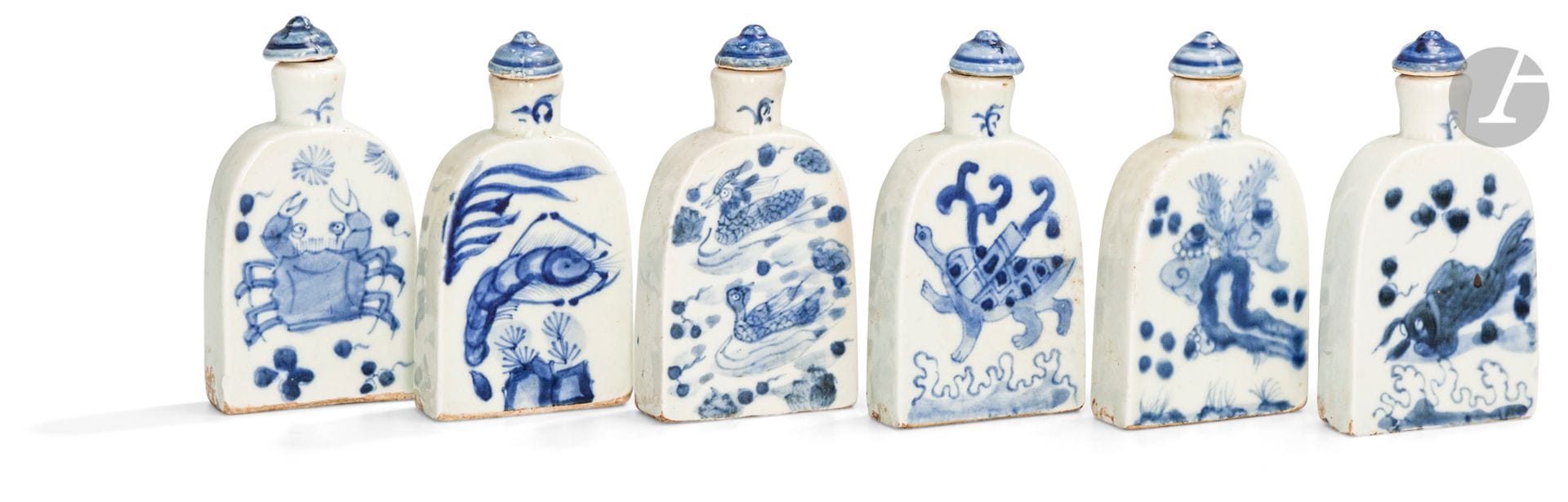 Six flacons à médecine en porcelaine bleu et blanc dans leur coffret, Chine, début XXe siècle
En forme de cloche aplatie, émaillés en bleu sous couverte d’une crevette, d’un crabe, de deux canards mandarins, d’un poisson, d’une tortue et de coquillages. Seule une petite marque en bleu orne les revers laissés en blanc. Les bases rectangulaires non émaillées et les bouchons en porcelaine émaillée en bleu.
Hauteur : 9 cm