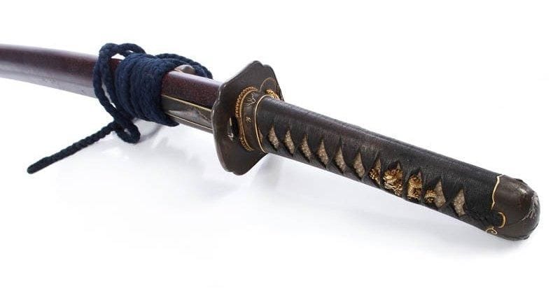 Wakizashi shinogi zukuri, hamon suguha gravé d'un dragon et d'un ken. La fusée percée d'un mekugi ana et portant la date de Kanbun 13 (1673). Signée Tomotsugu en damasquiné or. Nagasa. Fourreau en laque brun avec kozuka à décor du mont Fuji. Long.: 54 cm