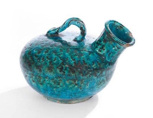 RARE GARGOULETTE, IRAN, ART SAFAVIDE, XVIIe SIÈCLE Céramique siliceuse à panse lenticulaire sur base annulaire, à col à pans coupés relevé, et à anse tressée. Décor moucheté noir sous glaçure turquoise. H.: 16 cm et long. 20 cm Petits éclats au rebord et sur la panse L'association de ce décor et de ce type de forme est, à notre connaissance, tout à fait exceptionnelle. Pour ce qui est de la forme, relativement rare dans le répertoire islamique, on en connaît surtout des exemples à décor moulé non glaçuré, plus rarement à glaçure monochrome, d'époque seldjoukide et il-khanide (voir Metropolitan Museum of Art, n°38.40.146, ou encore Christie's Londres, 16 octobre 2001, lots n°246 et 247). On note néanmoins la présence dans les collections du Louvre, sous le numéro d'inventaire MAO 1203, une gargoulette à décor bleu et noir sur fond blanc de motifs épigraphiques et végétaux, datées du XIVe siècle qui témoigne de l'utilisation de ce type de pièce comme support d'un décor peint sous glaçure. Dans le cas présent, ce décor moucheté sous glaçure turquoise rappelle un plat au même décor mouché conservé au Louvre, sous le numéro d'inventaire MAO 658. Voir sur ces questions, MAKARIOU Sophie, Nouvelles acquisitions, Arts de l'Islam 1988-2001, Paris, RMN, 2002, n°13, ainsi que - MELIKIAN-CHIRVANI Souren, L'art de l'Iran safavide (1501-1736): le Chant du monde, Paris, RMN, 2007