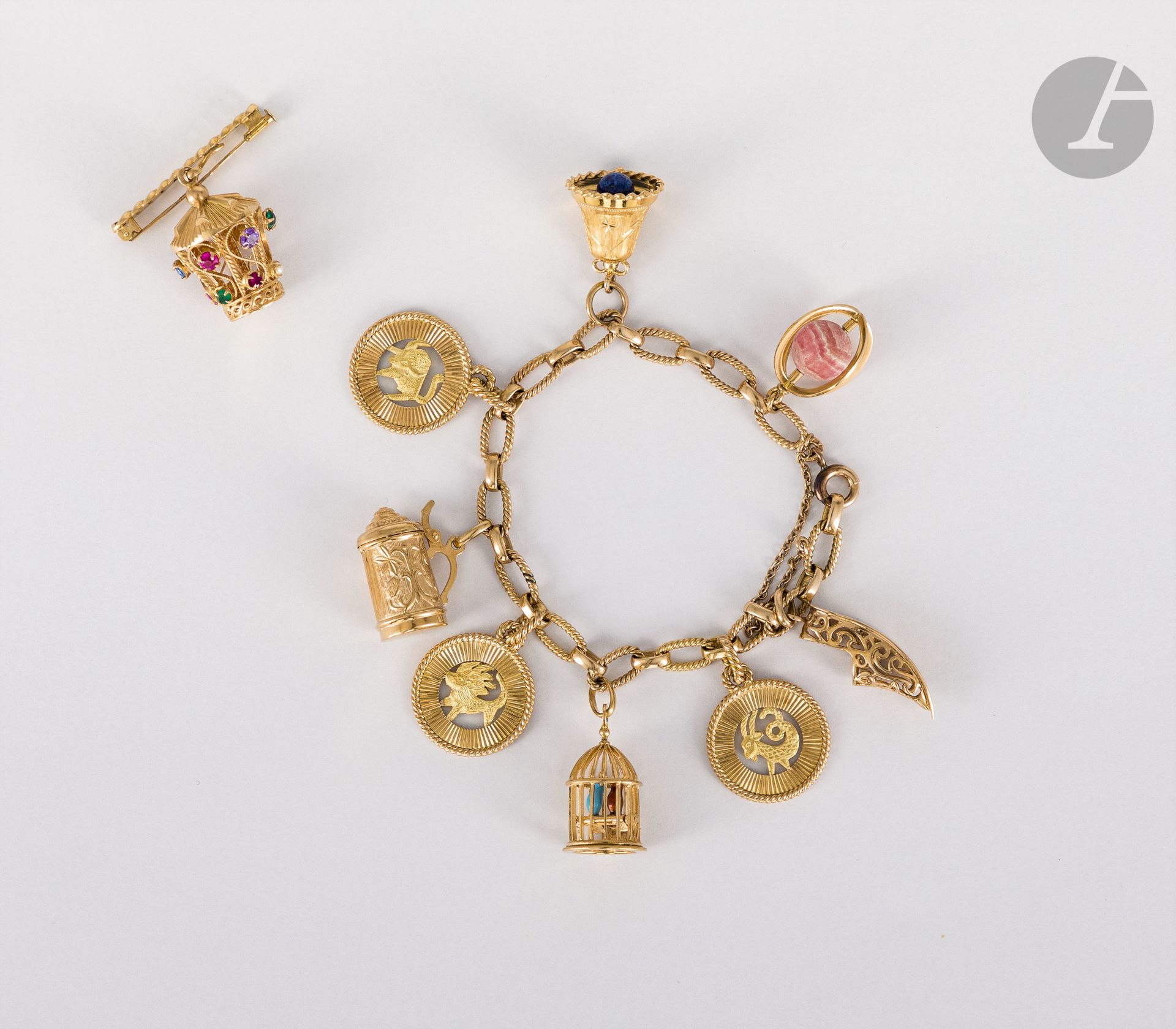 Bracelet en or 18K (750), orné de pampilles en or 18K (750) : une babouche, 3 médailles astrologiques (capricorne, lion et taureau), une cage habitée d'oiseaux, une chope, une clochette et une sphère de rodhocrosite. Poids brut : 53,3 g (on joint une broche en or 18K, ornée d'une pampille  lanterne sertie de pierres fantaisie)