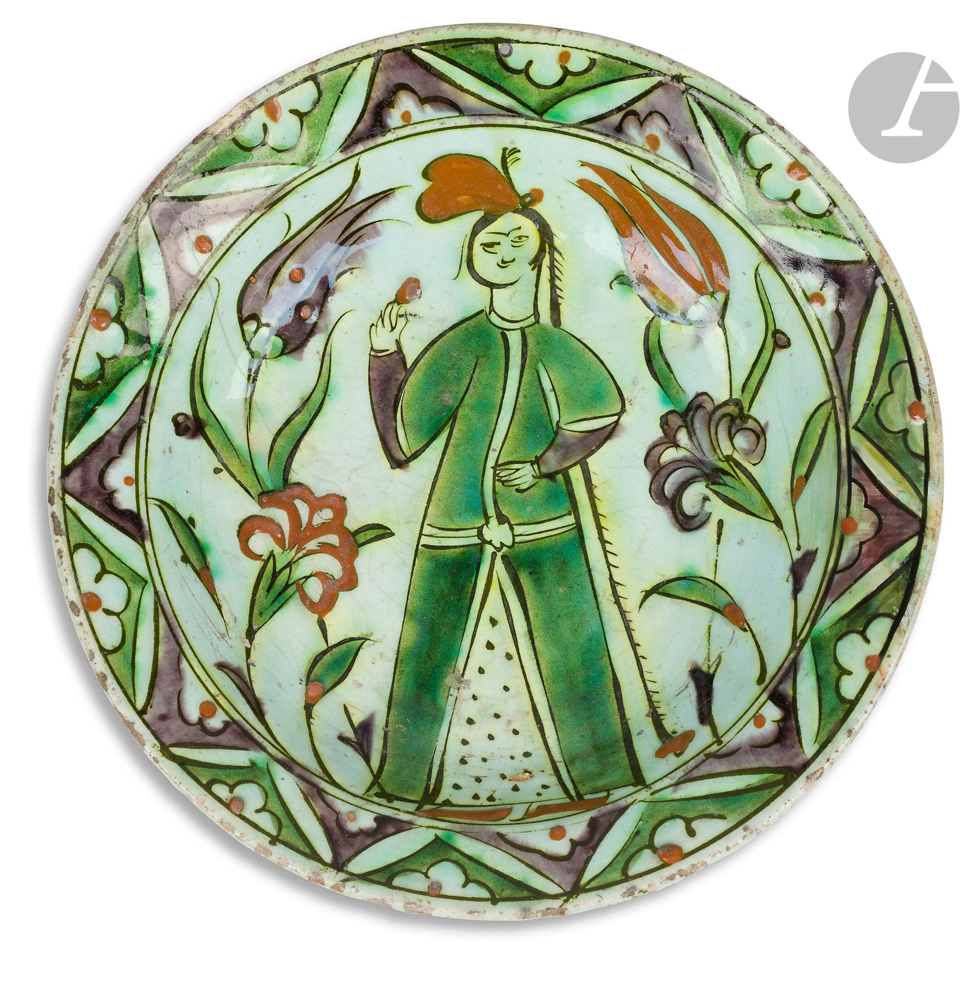 Plat tabak à décor de femme dans un jardin, Turquie ottomane, Iznik, XVIIe siècle
Plat en céramique siliceuse à décor peint sous glaçure transparente d’une femme vêtue d’un long caftan vert et coiffée d’une longue natte s’échappant d’une coiffe rouge, reniflant une fleur dans un jardin de tulipes et d’œillets. Marli à décor de chevrons abritant des demi-rosettes.
Diamètre : 25,8 cm
Trous de suspension, fêles, éclat, restaurations

Ce plat est à rapprocher tant par le sujet que par la coiffure de la femme ou le décor du marli du plat inv. 19565 du Musée National de la Céramique de Sèvres en dépôt au Musée du Louvre sous le numéro OA 3914.

A tabak dish with a woman in a garden, Ottoman Turkey, Iznik, 17th century
