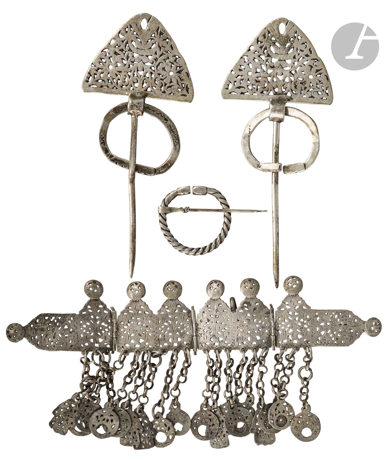 Diadème jbin et trois fibules, Tunisie, début XXe siècle
- Le diadème, probablement de Tajerouine, constitué de quatre plaques d’argent articulées en forme de fronton coiffé d’un disque à décor ajouré et ciselé et soulignées de pampilles en mains khamsa ou disques au bout d’une chaînette. Deux crochets latéraux. L. : 24,6 cm, P.B. : 184 g ; - les trois fibules khella, une paire à plaque moulée et ajourée munie d’un anneau plat et une fibule circulaire striée aux extrémités polyédriques, H. paire : 17,8 et 17,6 cm, légères déformations, D. fibule circulaire : 4,7 cm, P.B. : 145 g

A jbin diadem and three khella fibulae, Tunisia, early 20th century

Collection Éric N. Lasry