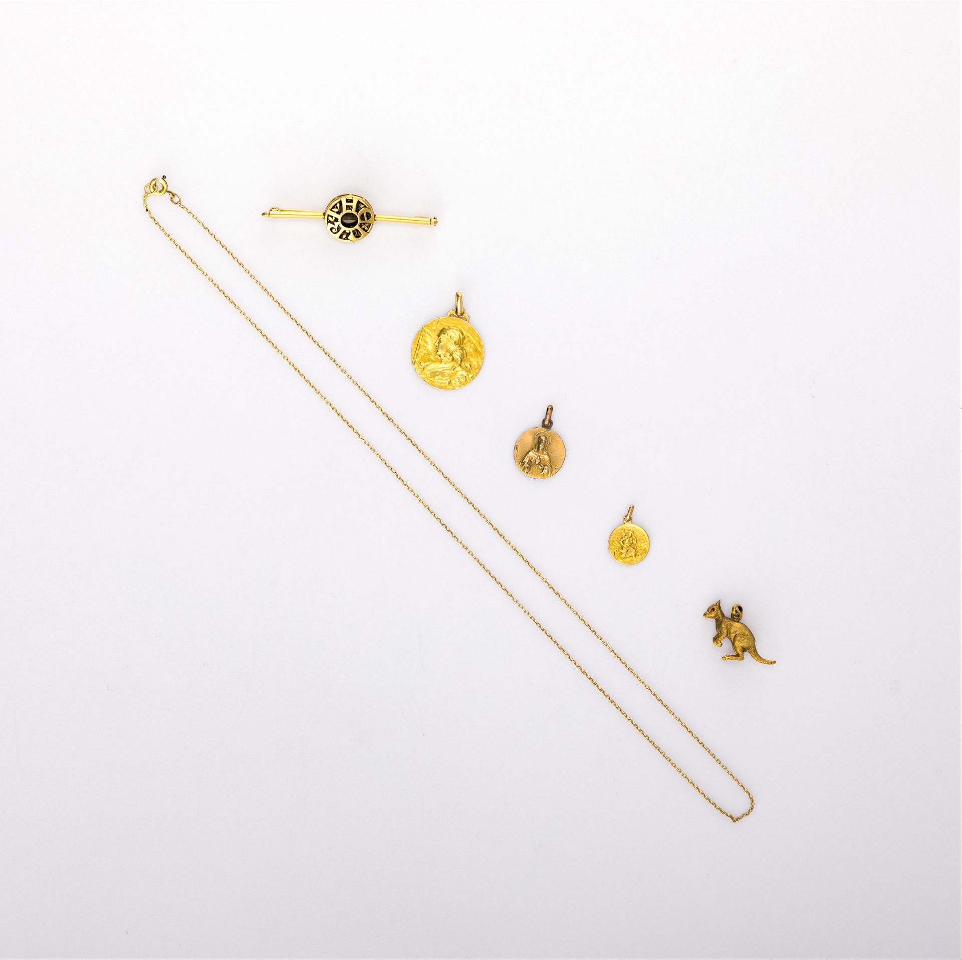 Lot de bijoux en or (18K et 22K). Poids brut: 17,2 g
- 1 chaine, 2 médailles, 1 broche barette, 
- 1 pendentif kangourou en or (22K), yeux en pierres rouges. Poids brut: 1,5 g
On joint une médaille religieuse en métal.