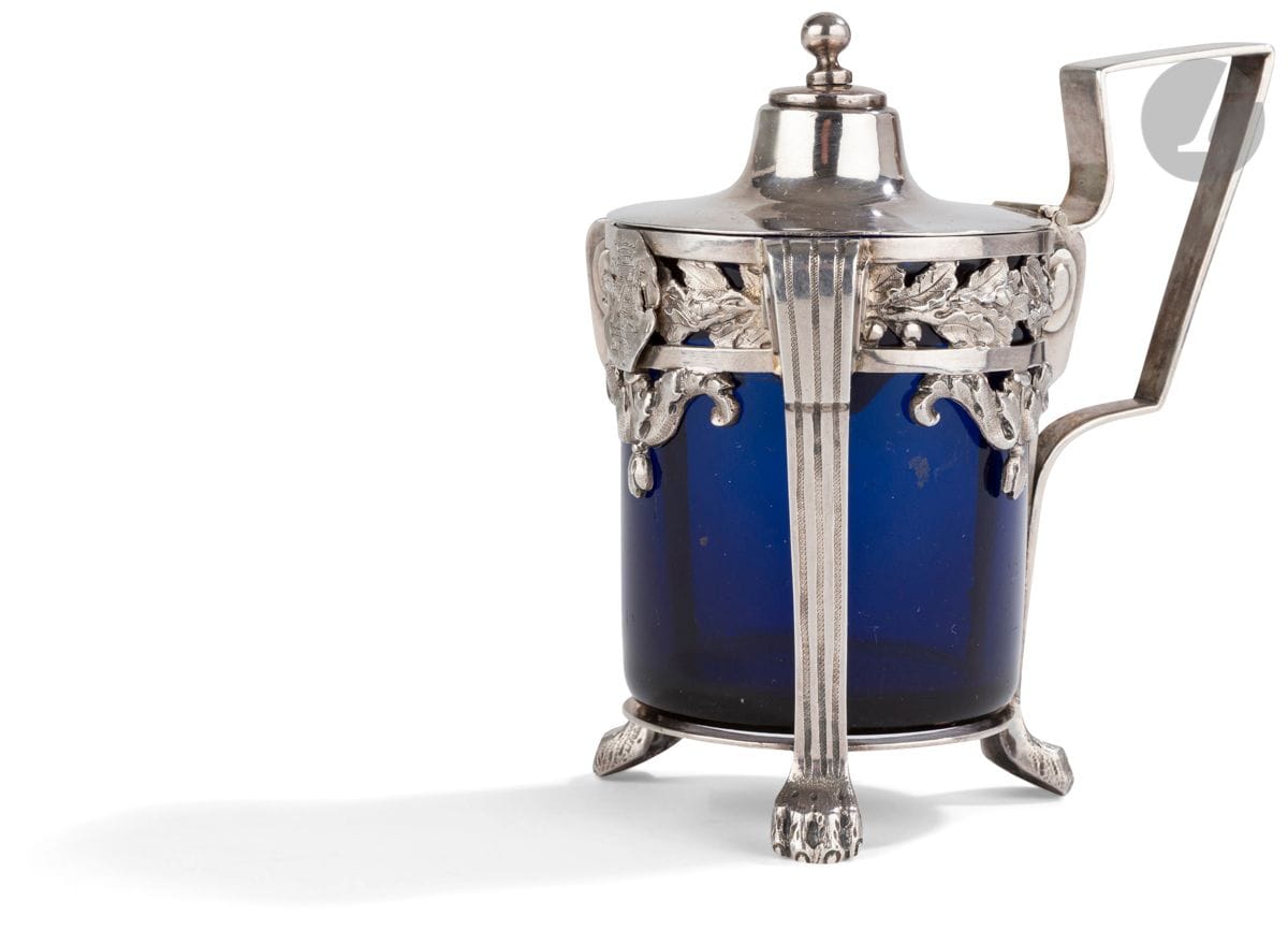 TOULOUSE DERNIER QUART DU XVIIIe SIÈCLE
Moutardier en argent fondu et un verre bleu. Il repose sur trois pieds pilastre terminés par des griffes. En bordure le décor est ajouré à l’horizontal de feuilles de chêne encadrées de guirlande en chute. Le couvercle à doucine est uni, sommé d’une prise bouton. Anse à la grecque. Armoiries rapportées.
Maître orfèvre : Antoine-Joseph LAFONT, reçu en 1789
Poids net : 200 g - hauteur : 11,8 cm
État : réemploi d’un couvercle ancien du XVIIIe siècle