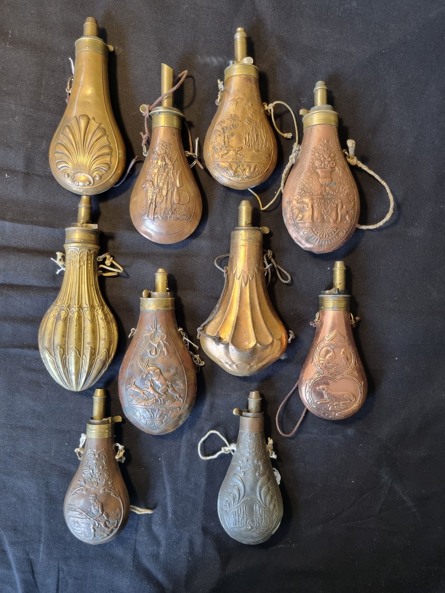 Lot of ten powder flasks 

in copper and brass, some with measuring spouts, decorated with hunting scenes and animals. 

19th century.