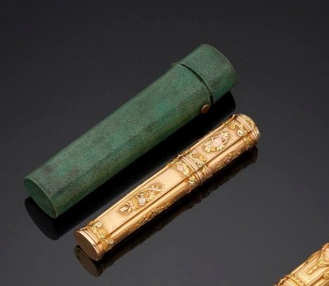PARIS 1762 - 1763
Étui à cire en ors de quatre couleurs : jaune, blanc, rose et vert, le talon non gravé dans son étui en galuchat. De section ovale quadrilobée, en deux parties, ciselé sur une face d’instruments agraires sur fond amati et d’instruments de musique sur l’autre face dans des encadrements ovales séparés par des bouquets de fleurs et de fruits. 
Maître orfèvre : Nicolas DURIER, reçu en 1758
Poids : 52,4 g - longueur : 11,5 cm
État : parfait état y compris de l’étui à charnière