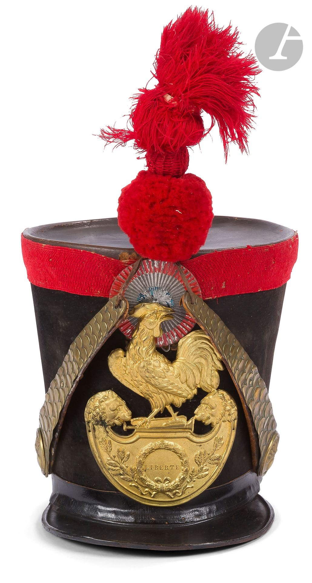 Shako de chasseur de la Garde nationale. 
Fût en carton recouvert de feutre taupé. Galon en passementerie écarlate. Calotte, bourdalou et visière en cuir verni. Plaque au coq à soubassement marquée « LIBERTE » en laiton doré. Rosaces à la grenade, jugulaires à fausses écailles doublées de cuir, en laiton. Cocarde tricolore en métal. Pompon flamme en laine écarlate. 
Coiffe intérieure en cuir, à dents de loups (usures).
B.E. Époque Monarchie de Juillet (1830-1848).