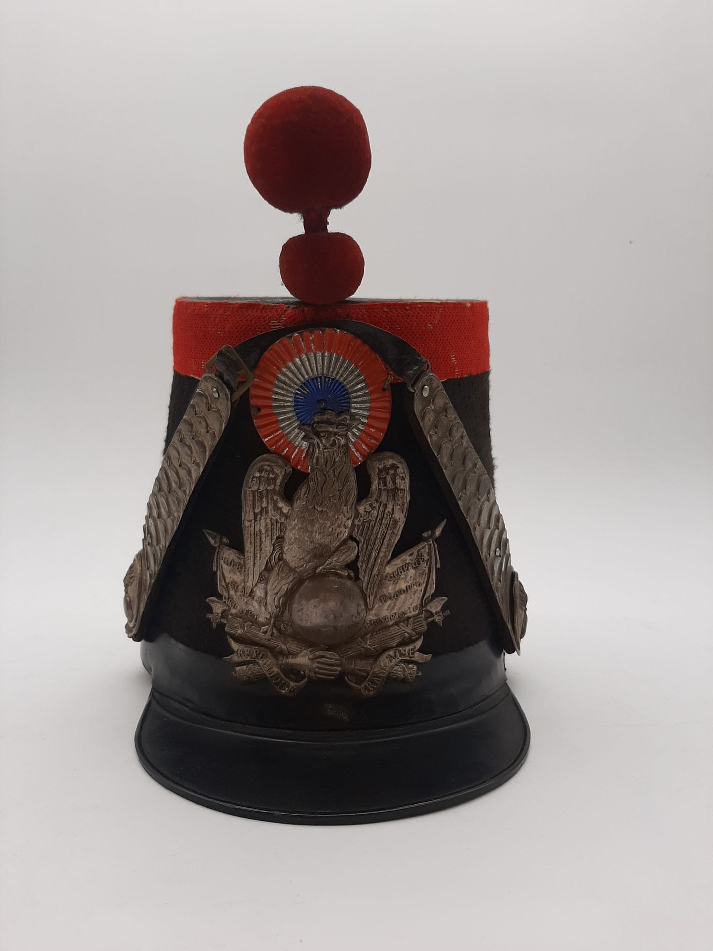 Shako d’officier de chasseur de la Garde Nationale. 
Fût en carton recouvert de feutre taupé. Calotte et visière vernies. Galon en passementerie d’argent, à lézarde et bourdalou en velours. Bossettes au cor, jugulaires à écailles doublées de velours et plaque au coq en cuivre argenté. Cocarde tricolore en métal. Pompon en laine jonquille. Coiffe intérieure à dents de loup.
B.E. Époque Monarchie de Juillet