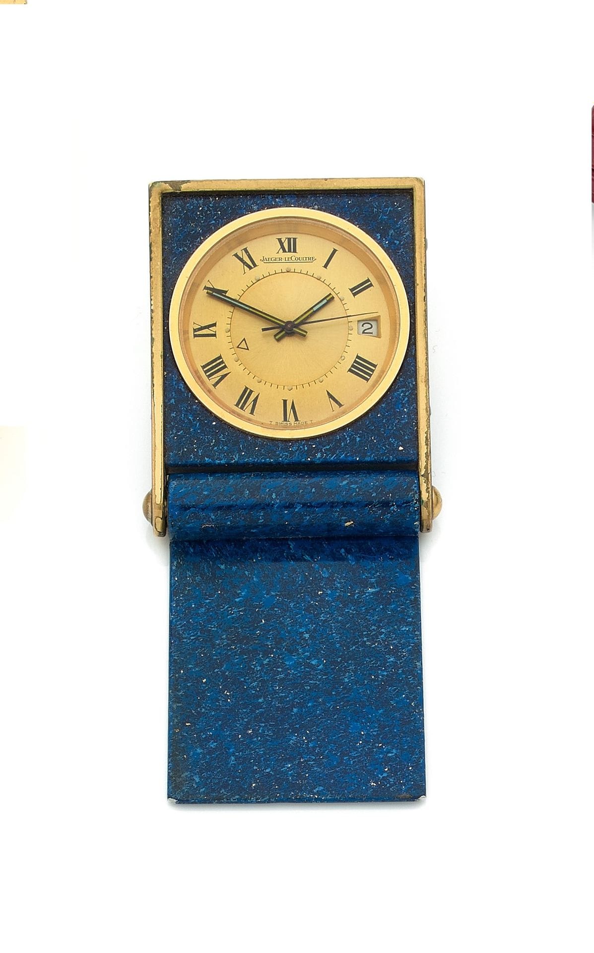 JAEGER LeCOULTRE. Vers 1980
N° 1270744
Pendulette en métal doré peinture façon lapis lazuli formant réveil, cadran doré, index chiffres romains formant les heures, date par guichet à 6H, disque central permettant de régler l’heure de réveil, mouvement à remontage mécanique.
Cadran, boîtier et mouvement signés.
Dimensions : 40 mm x 52 mm
