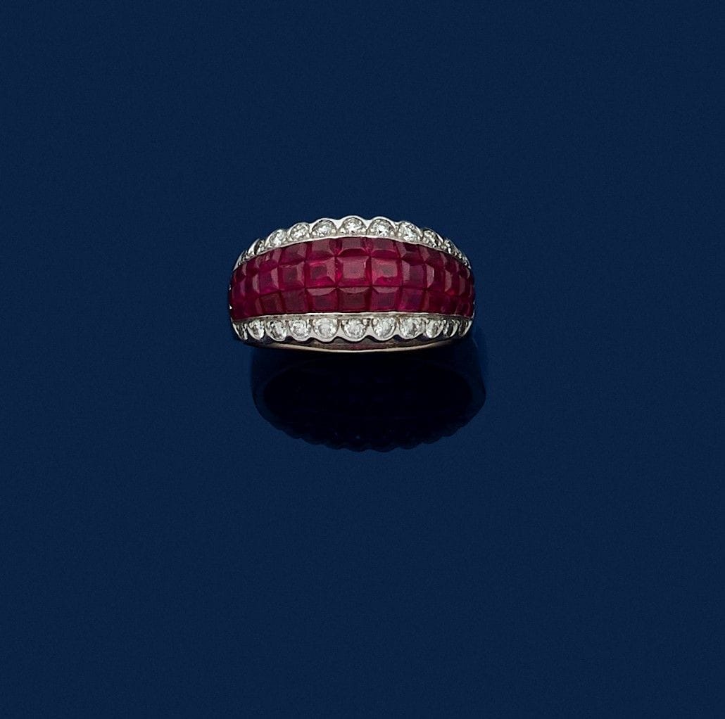 Bague en or gris 18K (750), ornée d’un bandeau de rubis calibrés entre deux rangs de diamants ronds de taille brillant festonnés. Tour de doigt : 54. Poids brut : 7,2 g (égrisures)

A ring set with rubies and diamonds