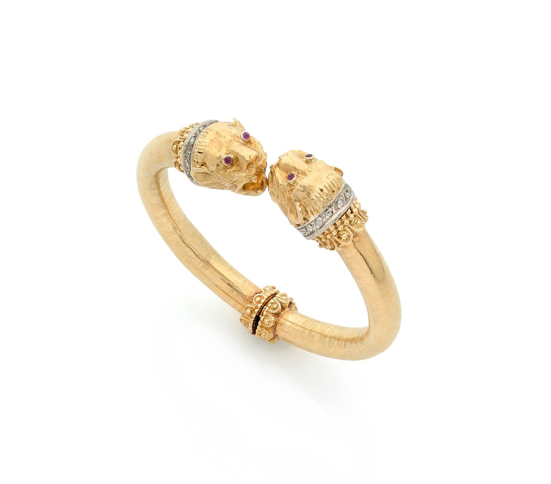 ZOLOTAS 
Bracelet articulé en or 18K (750) guilloché, les extrémités sculptées en protomées de lionnes, les yeux piqués chacun d’un rubis, les cous ornés de colliers de diamants taillés en roses sur platine. Monogrammé. Travail grec des années 1980. Conservé dans sa pochette. Longueur : 15 cm environ. Poids brut : 48,4 g

A Zolotas lion bracelet