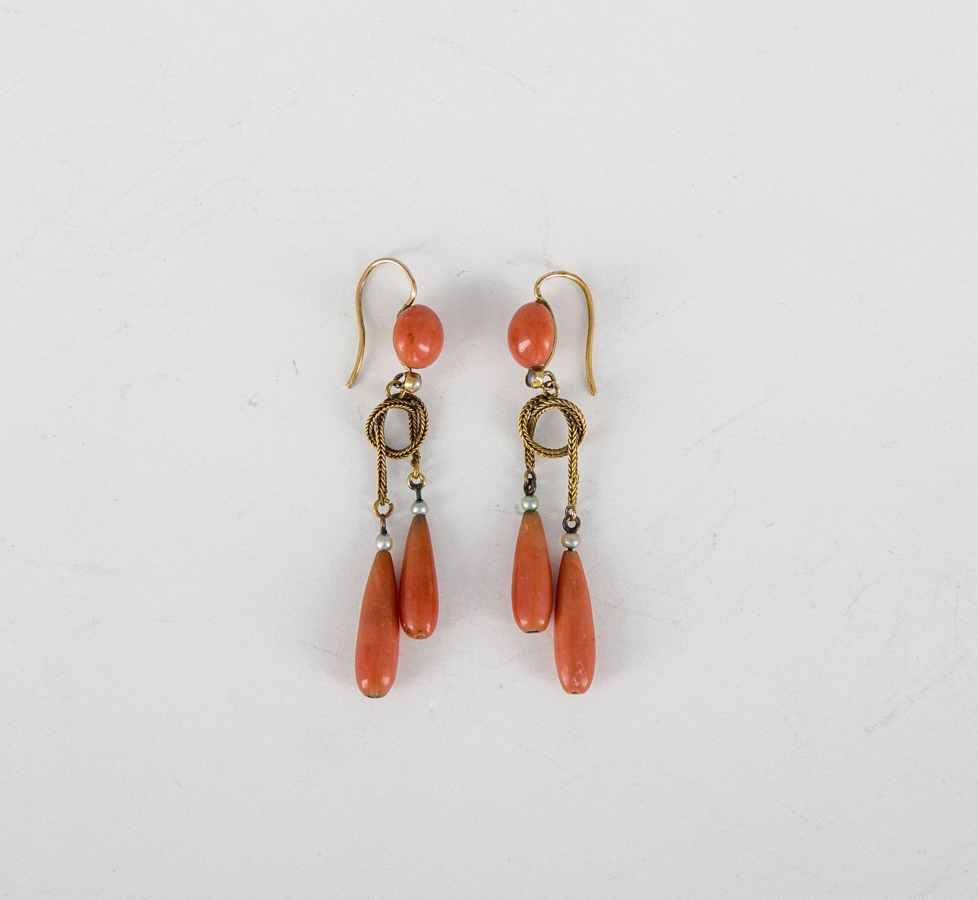 Paire de pendants d’oreilles en or 18K (750), ornés de pastilles et de gouttes de corail, agrémentés de petits perles sans doute fines. Travail français de la fin du XIXe siècle. Hauteur : 5,7 cm environ. Poids brut : 6,8 g (soudures, colle, fêles)

A French late 19th century ear pendents set with coral