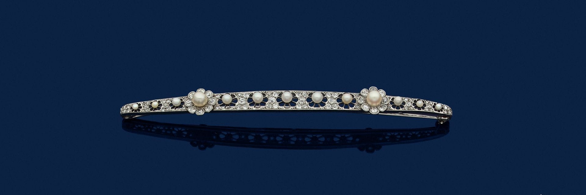 GEORGES FOUQUET
Grande broche-barrette en or gris 18K (750), ornée de perles dans des fleurs repercées, et de diamants de taille ancienne et taillés en roses. Signée et numérotée. Travail français des années 1910. Conservée dans son écrin. Longueur : 12 cm environ. Poids brut : 19,2 g

A 1910 Georges Fouquet brooch set with pearls and diamonds