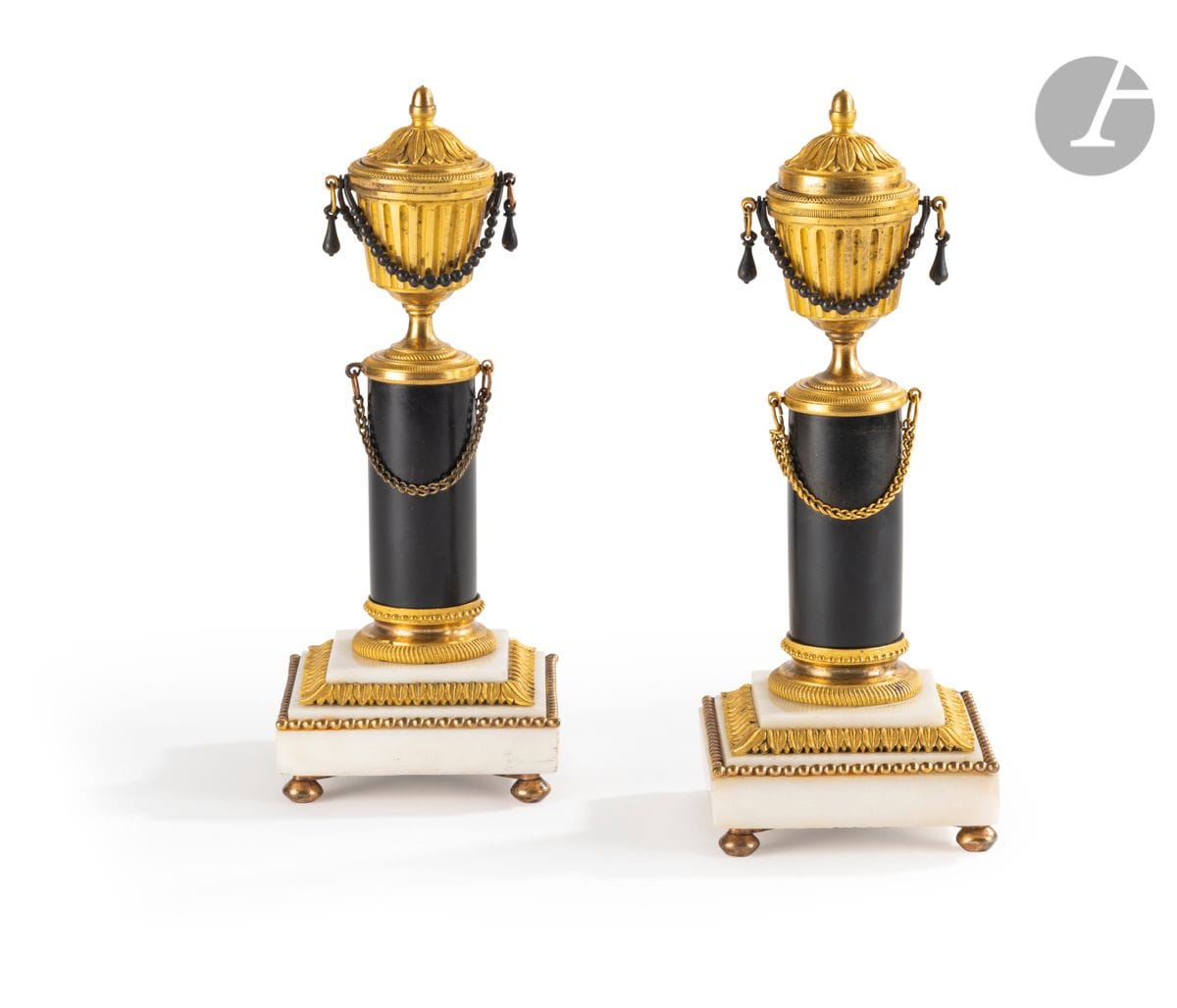 Paire de flambeaux en bronze patiné et bronze doré, le fût surmonté d’un vase à cannelures, le couvercle réversible formant bobèche, reposant sur une base en marbre blanc à décor de feuilles d’eau ; (usures). 
Époque Louis XVI.
H : 23 cm