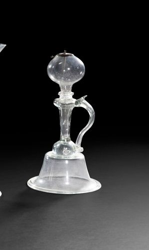 Lampe à huile ou veilleuse en verre soufflé, moulé en quatre parties, le pied en forme de cloche surmonté d’une jambe creuse, l’anse travaillée à la pince est rapportée. Le réservoir contient un porte-mèche en métal.
Petits accidents.
Provence, XVIIIe siècle.
H : 28 cm