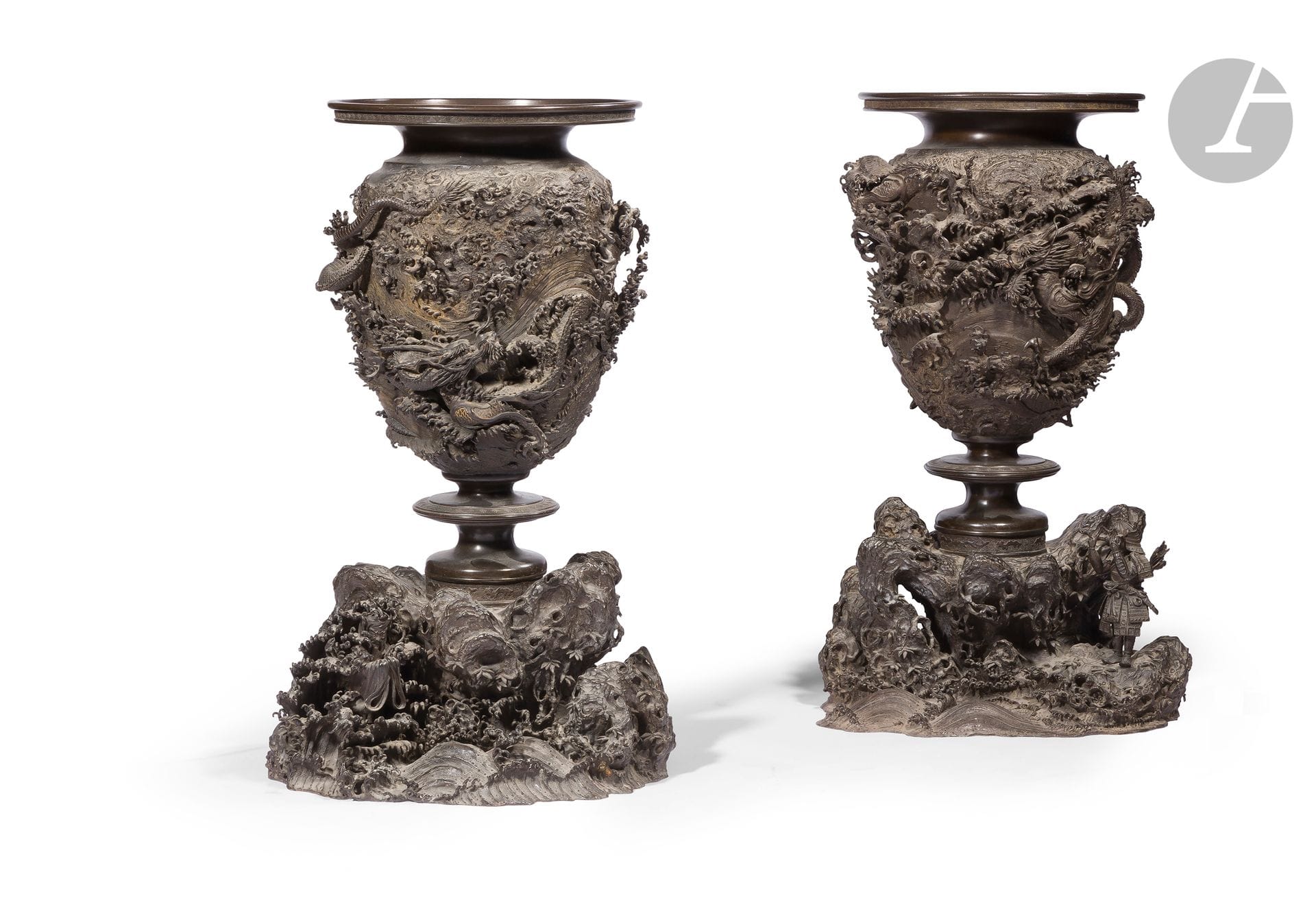 Paire d’importantes urnes en alliage de cuivre à patine brune à décor de la légende de Nitta no Yoshimasa, Japon, époque Meiji (1868-1912)
Chaque urne est fabriquée en trois parties, le haut est constitué d’un pavillon plat dont le rebord est à décor de frise de grecques. Il surmonte une panse ovoïde à décor en très haut relief de trois dragons dans les flots écumants, reposant sur un socle constitué d’un disque sur piédouche à décor de frise de grecques et de dragons stylisés, le tout fixé sur une base en forme de rochers et de végétations sortant des flots écumants. Au milieu des flots sur la gauche on reconnaît Ryujin, le roi de la mer, tandis que sur la base de l’autre urne, Nitta no Yoshimasa à Inamuragasaki apparaît dans son armure tenant son sabre devant le front alors qu’il va le jeter dans la mer en offrande à Ryujin, dans l’espoir d’une victoire contre les Hôjô. L’ensemble comporte deux signatures, l’une derrière un rocher sur la partie inférieure : Kinryusaï Gidô - 金龍斎義道造 (Suhara Yoshimichi) et une autre Judô (Hisamichi) zo - 壽 道造 - « fait par Judô » en caractères tensho (sigillaire) sous la partie supérieure.
Hauteur totale : 59 cm
Quelques manques, un fond ressoudé.

S’engageant dans la campagne de Kamakura de 1333 pour vaincre le clan Hôjô sur ordre de l’empereur Go-Daigo (1288-1339), Nitta Yoshisada (1301-1338) se trouva dans une impasse insurmontable. Bloqué par la forteresse naturelle que constituent les pentes vertigineuses de Kamakura et la flotte des Hôjô disséminée le long des caps, obéir à l’ordre de l’empereur nécessitait un évènement hors du commun. Yoshisada se plaça sur le rivage et regarda vers l’océan, priant le dieu dragon Ryujin, le tout puissant régent des mers. Il jeta ensuite son sabre dans l’eau. Répondant à son appel, le dieu dragon fendit la mer, permettant à Yoshisada d’atteindre la forteresse Hôjô.


