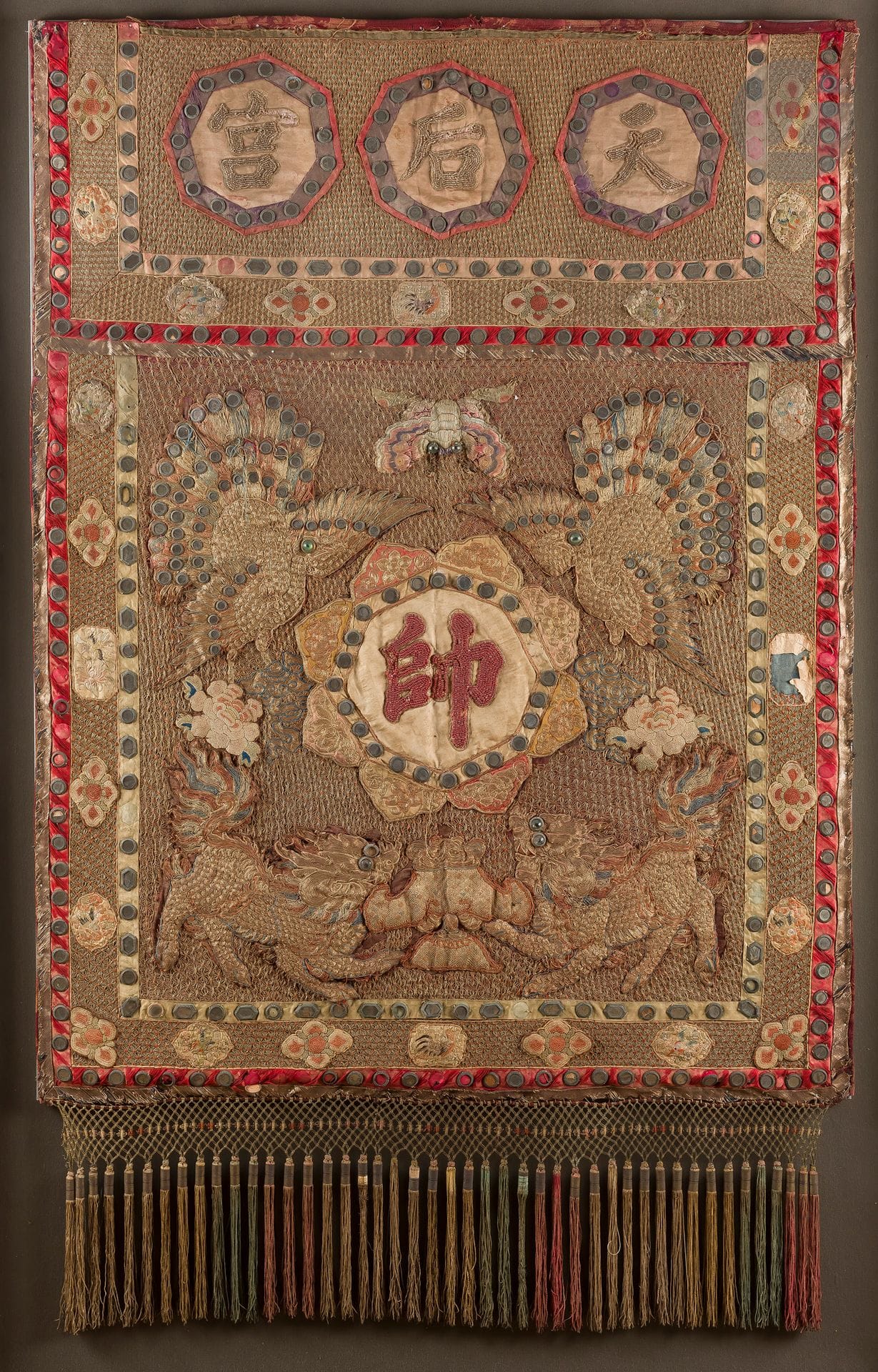 Embroidered silk high banner for Mazu worship-妈祖, Canton, China, late 19th-early 20th centuryIt
is formed of two parts embroidered with gold metallic threads and polychrome silks. The upper part shows three octagonal-shaped cartouches enclosing the three characters 天 后 宫 - Tian hou gong, "Temple (Palace) of the Queen of Heaven (Mazu)", formed by small white glass beads, strung and embroidered. The lower part is embroidered in the center with an eight-petal flower with the character 帅 - shuai (army general) in the middle in small red glass beads. All around, two qilin, two peony flowers, two peacocks and a butterfly. The eyes of the animals, the plumage of the peacocks, the flower and the borders of the banner are embellished with half-spheres of colored glass or small mirrors circled with metal. The borders of the textile are decorated with medallions of various birds and flowers and the bottom with a beige silk net from which are suspended tassels of multicolored silk. This banner was probably used in temples during representations related to the Mazu cult.
143 x 90 cmWear
, discoloration and missing parts

.

Fixed on a panel in a frame.

Originally the protector of sailors, Mazu is a Chinese goddess who originated in the 10th century and whose cult extends mainly along the southern and eastern coasts of China as well as in Macao, Taiwan and Hong Kong. At the center of a multitude of beliefs and customs, including oral traditions, religious ceremonies and traditional practices, the Mazu cult is inscribed on the Representative List of Intangible Cultural Heritage of Humanity.

十九世纪晚期-二十世纪早期 彩金线刺绣钉珠丝织天后宫帅旗






