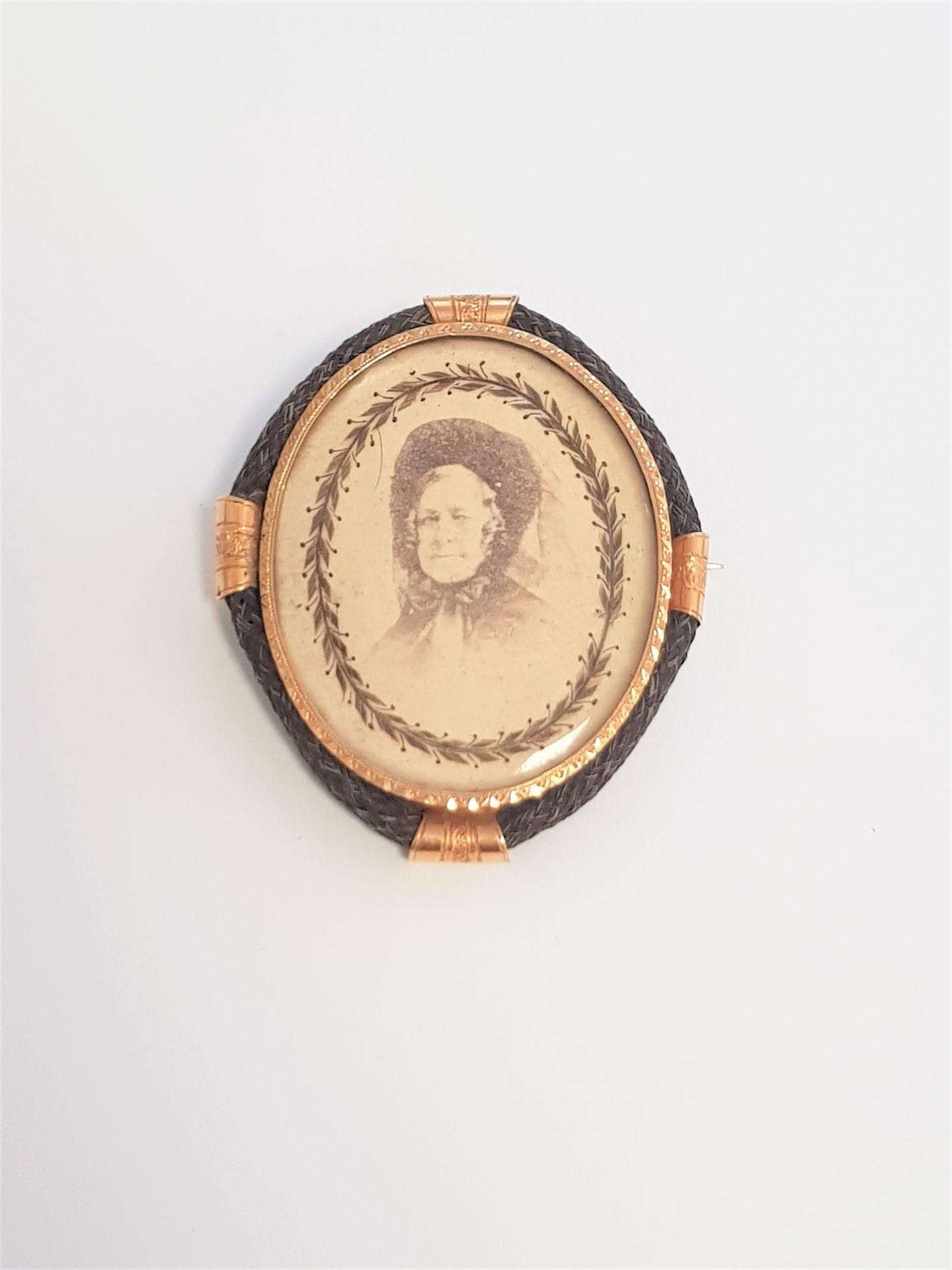 Broche en or 18K (750) recélant un portrait de femme dans une frise de cheveux, la monture en cheveux tressés. Travail du XIXe siècle. Hauteur : 4,5 cm environ. Poids brut : 13,5 g