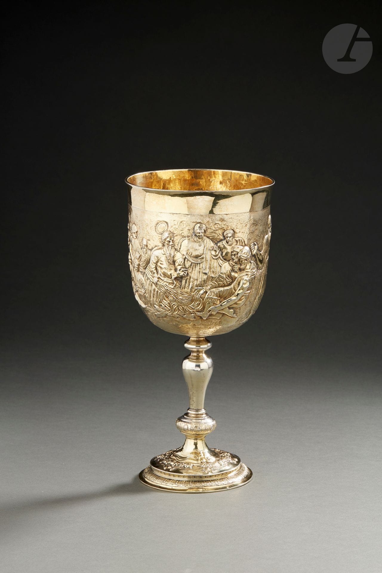 LONDON 1697
Large vermeil cup resting on a baluster foot. The pedestal is bordered with gadroons extended on the doucine of a repoussé decoration of fruits on an amati background. The cup features several characters framing Christ on a lake background - probably the Lake of Tiberias - during the miracle of the multiplication of the loaves. 
Master goldsmith : Francis GATHORNE 
Weight : 465 g - height : 26 cm
Condition : slightly worm-eaten in the central part of the foot