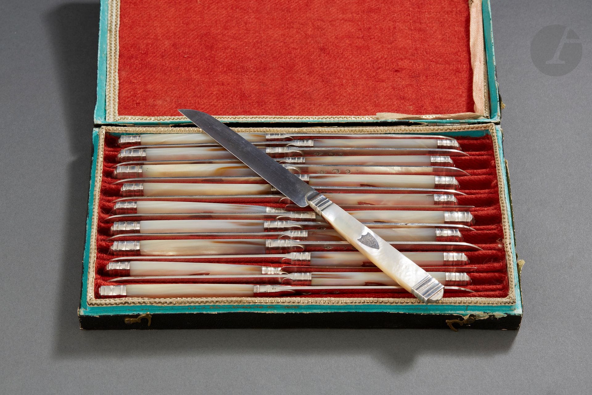 PROVINCE 1809 - 1819
Série de dix-huit couteaux à fruits, les manches à nacre, les lames en argent, monogrammé de lettres entrelacées dans un écusson, dont douze attribués à LANGRES dans un écrin doublé de tissu rouge. 
Orfèvre ou maître coutelier marquant des initiales MF.
Poids : 495 g - longueur : 19,5 cm