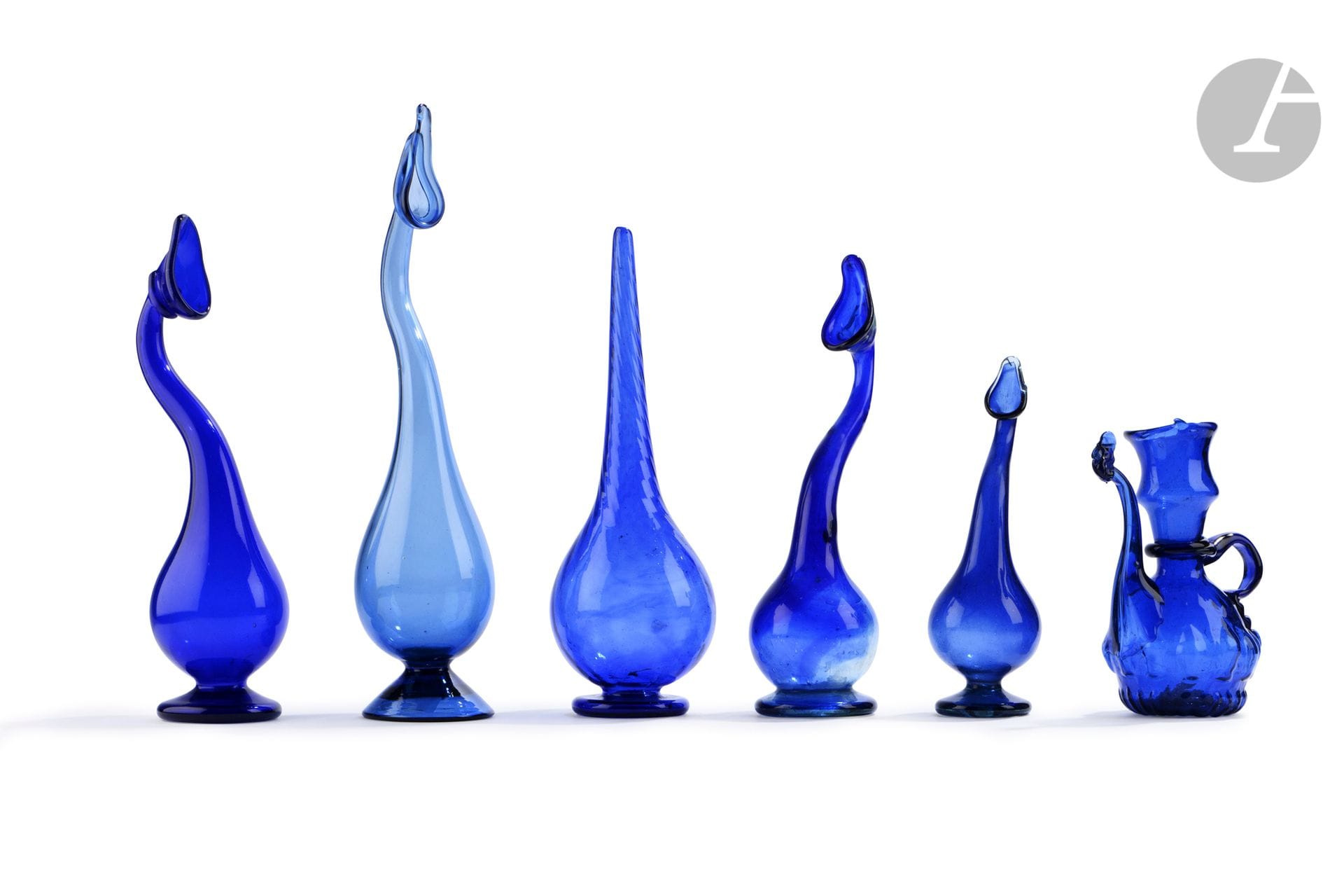 Six glassworks, Iran, 19th-20th century
In blue blown glass, a pourer with a gadrooned body, a sprinkler with a long ribbed tapered neck and four elegant bottles with sinuous swan necks, one of a lighter blue.
Height : 17 to 35,3 cm

According to poetic tradition, swan-necked bottles were used in Iran as lachrymatory vessels or "tear vessels" ("ashkdan") to collect the sorrows of wives separated from their husbands.

Six Blue Glass Vases, Iran, 19th - 20th century