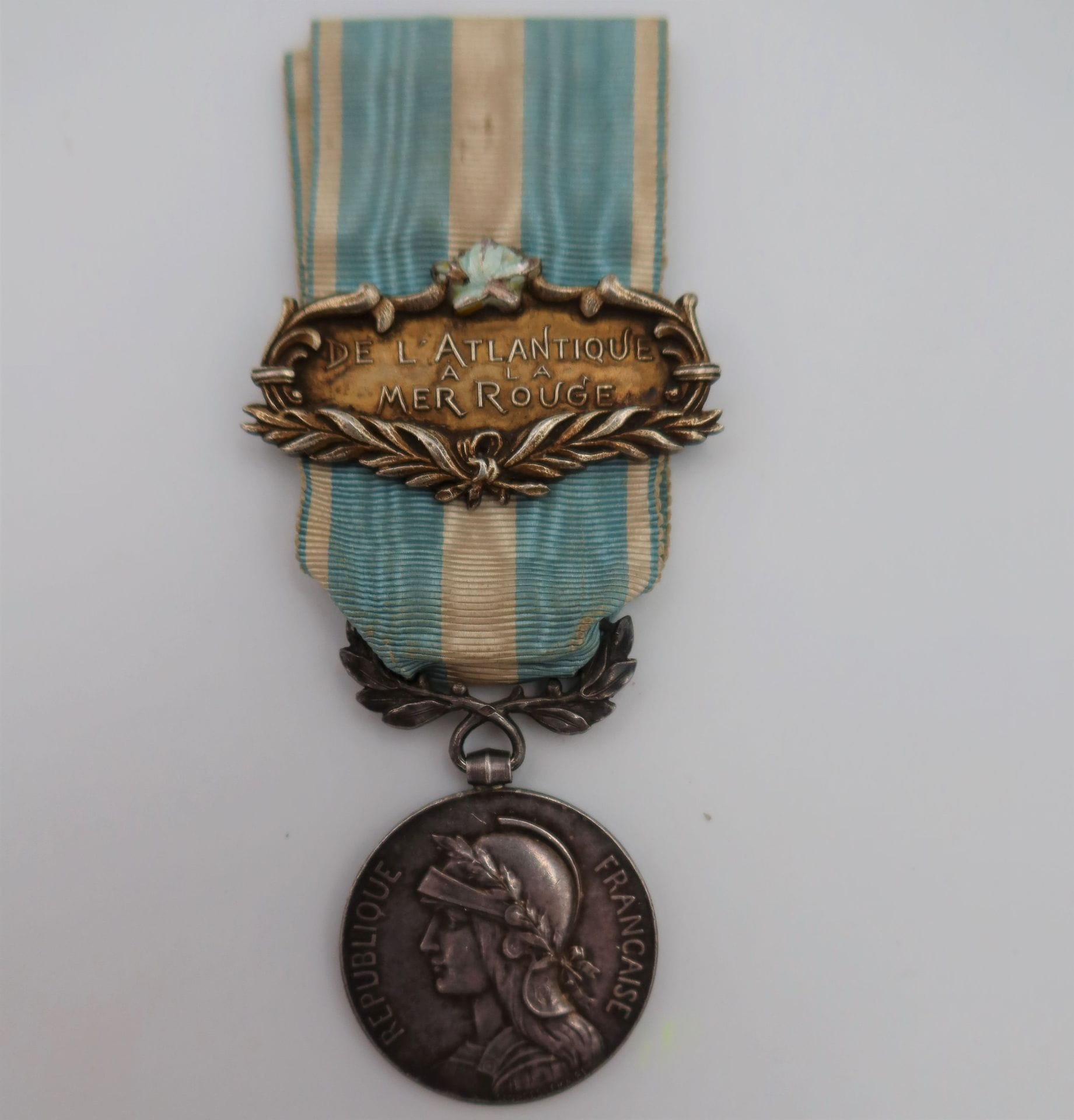 FRANCE 
MÉDAILLE COLONIALE (1893)
DE L’ATLANTIQUE À LA MER ROUGE. 
Médaille coloniale du 1er type. Jeton poinçonné de la Monnaie de Paris (Argent corne d’abondance). Bélière poinçonnée de Mercier. 
Ruban à belle agrafe à clapet, en vermeil, modèle attribué au fabricant « Lasne-Bacqueville, marqué « De l’Atlantique à la mer rouge » dans un encadrement de feuillages et palmes, surmonté d’un motif feuillagé émaillé bleu clair (éclats).
Poids brut : 29,6 g
T.T.B.
