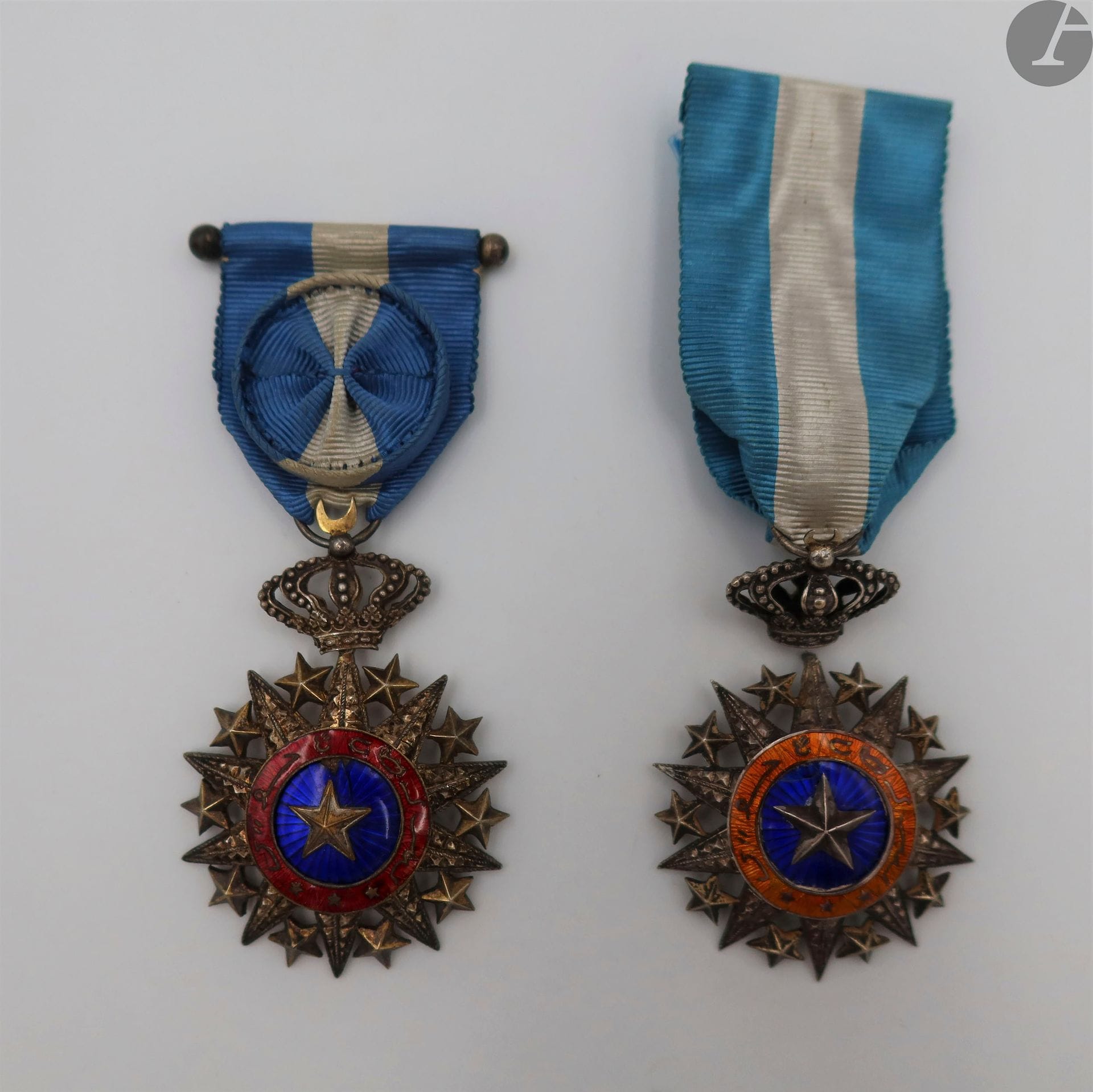 TADJOURAH
ORDRE DU NICHAN EL ANOUAR, créé en 1887.  
- étoile d’officier en argent, vermeil et émail. (éclats)Légende sur fond d’émail rouge.
Poinçon tête de sanglier. Ruban à rosette.
66 x 45 mm - Poids brut : 21,2 g
- étoile de chevalier en argent, vermeil et émail. (éclats, réparation à la jonction de l’étoile et de la couronne) Légende sur fond d’émail orangé. Poinçon tête de sanglier. Ruban.
66 x 45 mm - Poids brut : 20,3 g
T.B. à T.T.B.