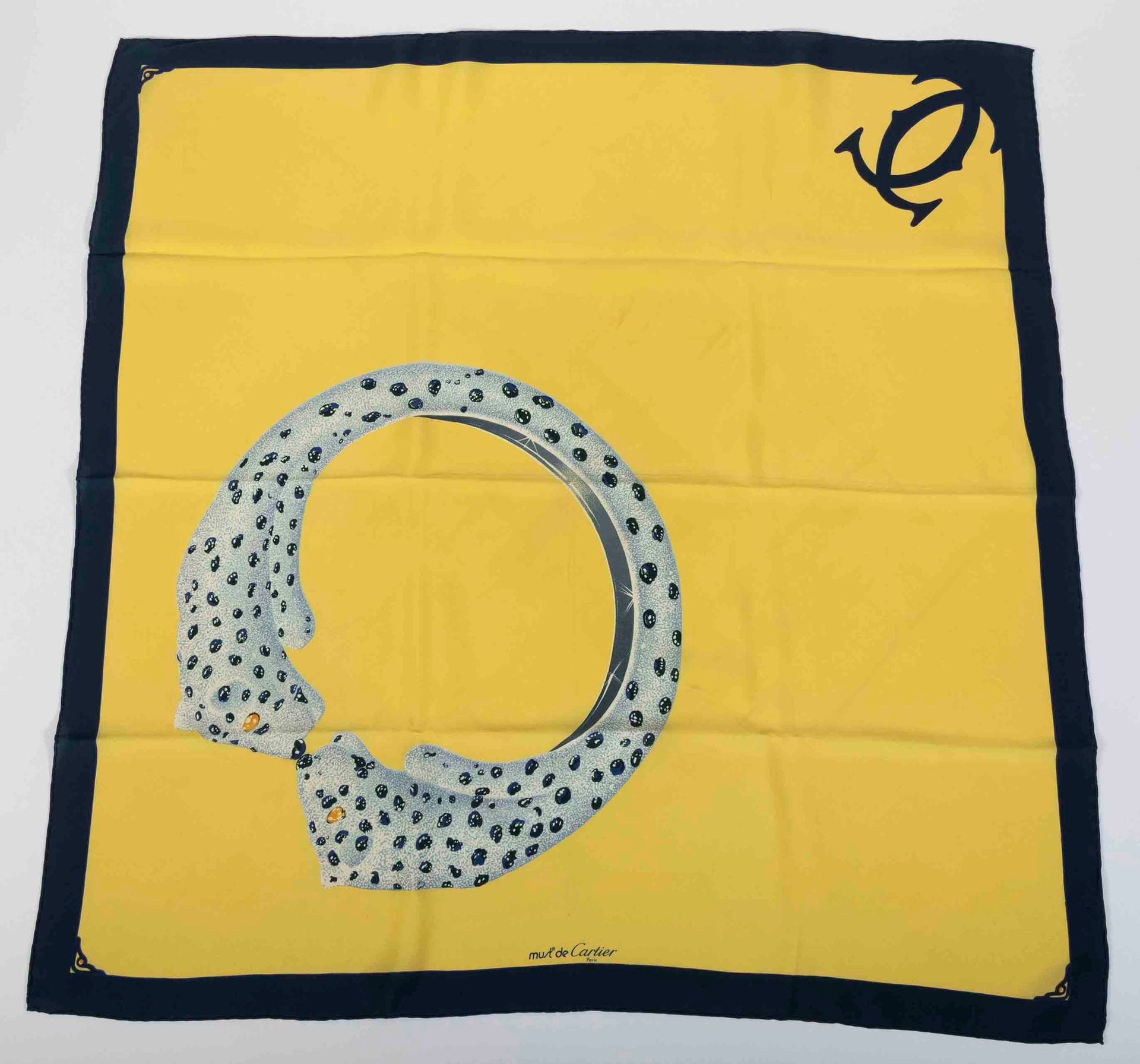 Must de CARTIER
Foulard en soie à décor de la bague Panthère, fond jaune et entourage marine