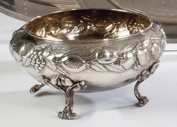 Coupe ronde en argent posant sur quatre pieds, les attaches feuillagées, le corps décoré en repoussé de guirlandes de fruits. Sterling. (Pied légèrement faussé) Diamètre: 30 cm Poids: 1,465 kg