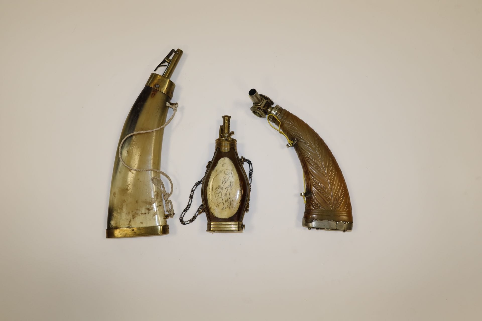 Lot de trois poires à poudre en corne à bec et garnitures laiton. 
Dont une à décor gravé de Diane, une unie, une sculptée d’épis de blé.
