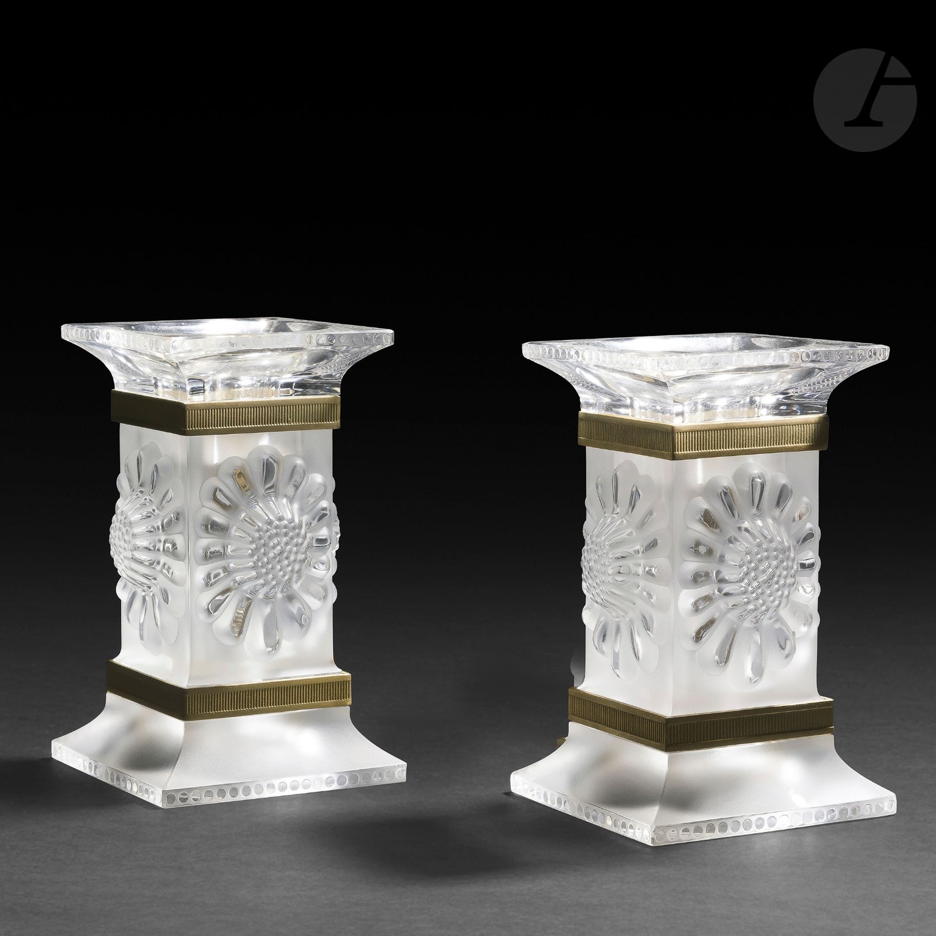 MAISON LALIQUE
Paire de bougeoirs. Épreuves en cristal moulé-pressé, et en partie satiné ; les montures en métal doré. Chacun doublement signé LALIQUE ® France en lettres cursives, à la pointe sous la base. Chaque bougeoir : H. 13 cm – L. 8 cm – l. 8 cm