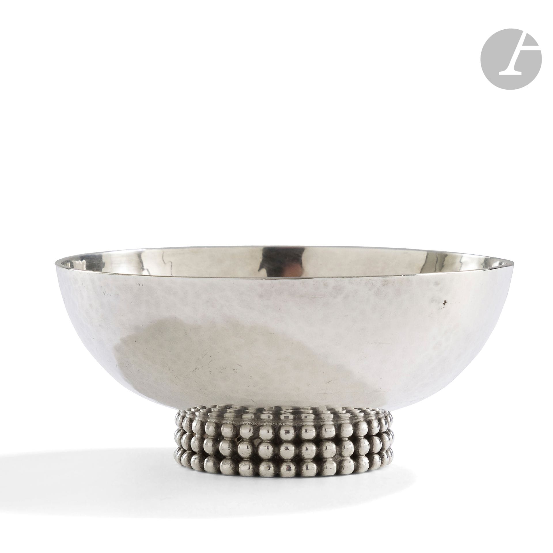 JEAN DESPRÉS (1889-1980)
Coupe circulaire sur talon en métal argenté à surface martelée. La base ornée d’une triple rangée de perles en application. Signée J. DESPRÉS à la pointe au revers. H. 4 cm – D. 9 cm