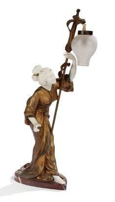 Adolphe Armand TRUFFIER (actif entre 1890 et 1930)
La geisha au lampion Lampe en composition patinée or et argent. La tête, les mains et le pied visible en biscuit. Lampion en verre. Terrasse en marbre. Manque l'extrémité d'un doigt, tête à refixer, altérations à la patine. Époque Art Nouveau, vers 1900. Signé Ad. TRUFFIER sur le bas du kimono. Hauteur: 50 cm