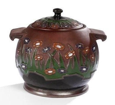 TRAVAIL ALLEMAND
Importante bol à punch en sphère aplatie reposant sur un talon en débordement et à deux anses formant prises. Épreuve en grès brun au décor tournant émaillé polychrome d'une frise de marguerites sur la panse et sur le couvercle. L'intérieur également émaillé. Quelques infimes égrenures éparses. Porte le monogramme lettré S.T entrelacés, le numéro 1453 et la mention 5L sous la base. 23 x 27,5 x 23 cm