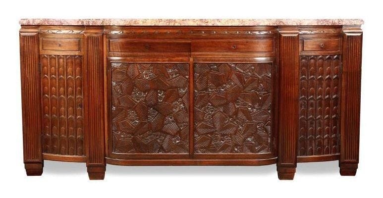 Paul FOLLOT (1877-1941)
Enfilade en palissandre teinté et entièrement monté sur chêne. La façade en double ressaut s'ouvre par deux tiroirs et par quatre portes au décor finement sculpté, les deux centrales de motifs géométriques et floraux en quinconce et les deux latérales de motifs façon écaille, et par deux tiroirs. Les montants sont au décor sculpté de larges cannelures et se terminent pour former les pieds. Dessus en marbre d'origine. Vers 1925 106 x 230 x 60 cm