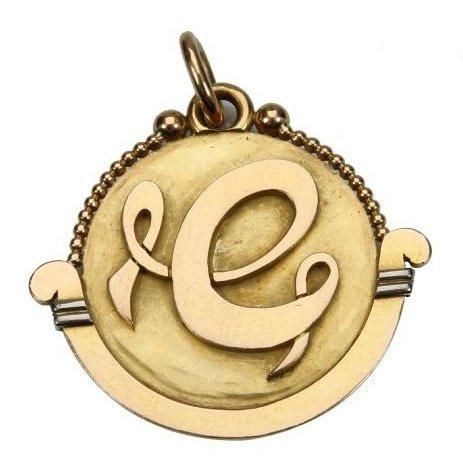 Jean DESPRES (1889-1980)
Rare pendentif double face en or. La lyre en corbeille, stylisée et terminée en enroulement aux extrémités, et ornée de double barrette en or blanc reçoit un disque achevé sur sa tranche de deux rangées perlées sommées d'une sphère. Une face au décor de volutes mêlées sur fond martelé, une autre présentant un monogramme stylisé à la ceinture perlée. Signée J. DESPRES à la pointe d'un côté et porte les poinçons de Maître titre sur la bélière. Poids: 32 g