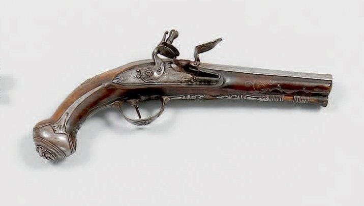 Pistolet à silex d'officier. Canon signé sur la bande «L. Lazarino», à méplats au tonnerre (raccourci). Platine signée «P. Martinoni» et chien col de cygne à corps ronds. Garnitures en fer découpé à jours. Canon, pontet, calotte et pièce de pouce ornés de masques grimaçants. Crosse en noyer décoré d'incrustations de fils d'argent. Baguette en bois à embout en corne. A.B.E. Italie, vers 1780. L. Lazarino Lazaro, Brescia. Martinoni Pietro, Lugano, Tessin Suisse et Brescia
